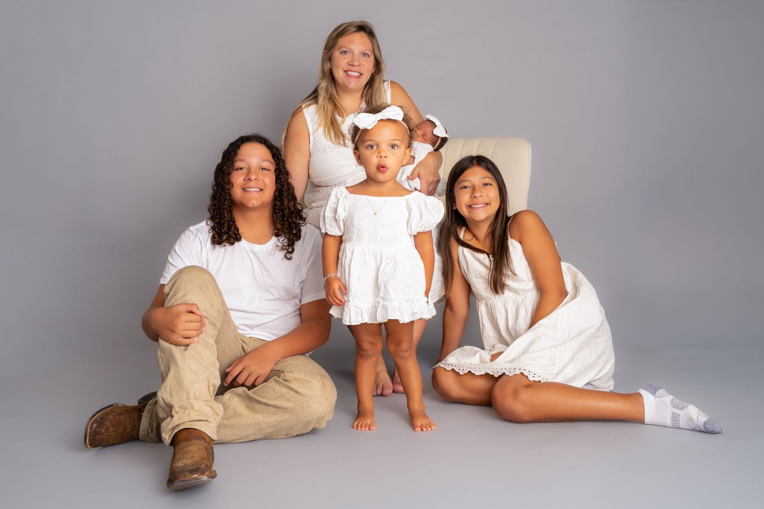 Family of four in white outfits posing for a studio portrait against a gray background.