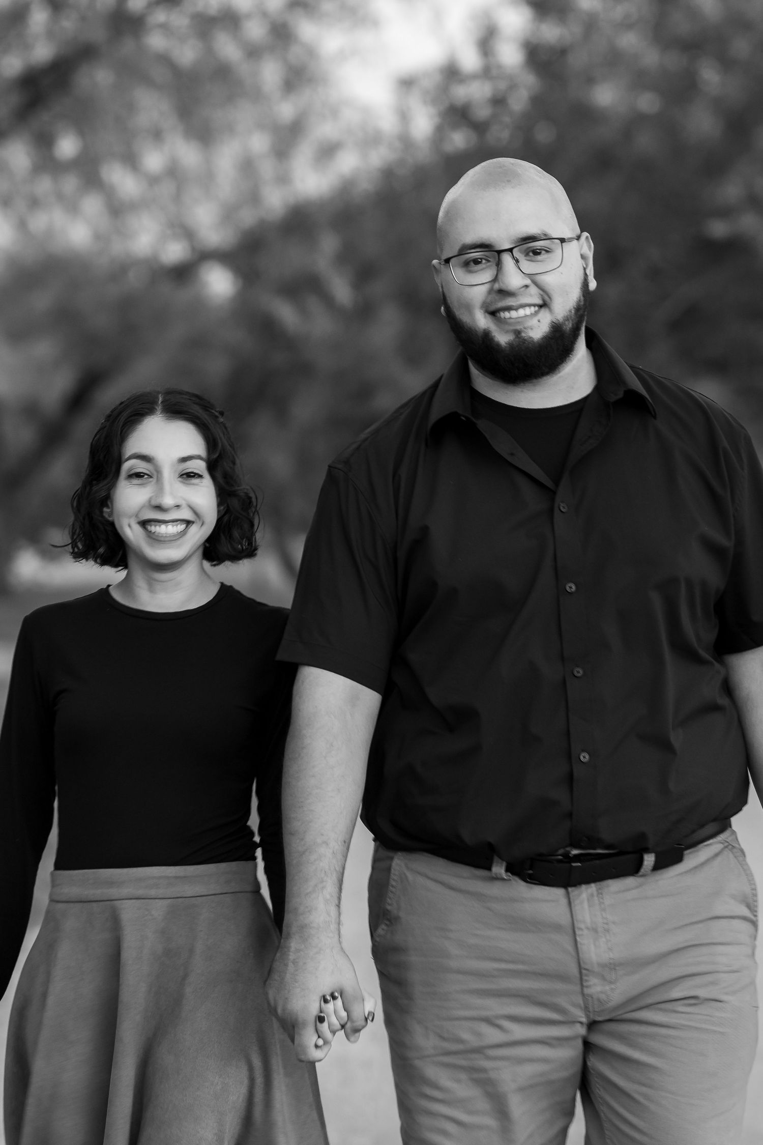 A black and white portrait of a couple standing together outdoors with a soft blurred background.