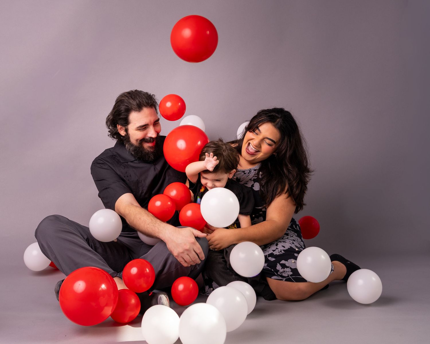 A couple playing with red and white balloons against a grey studio backdrop.