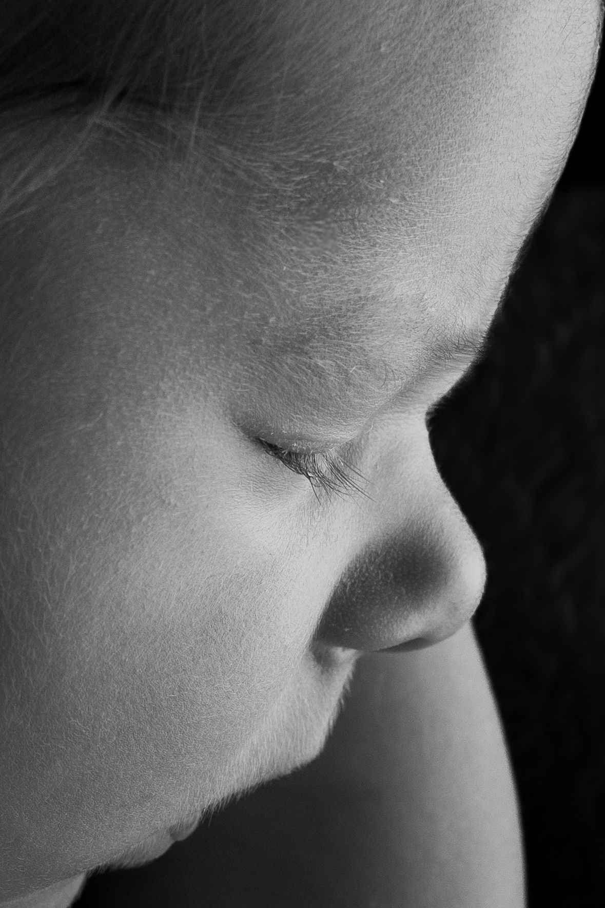 Black and white close-up profile portrait of a young child with eyes closed, soft skin texture visible.