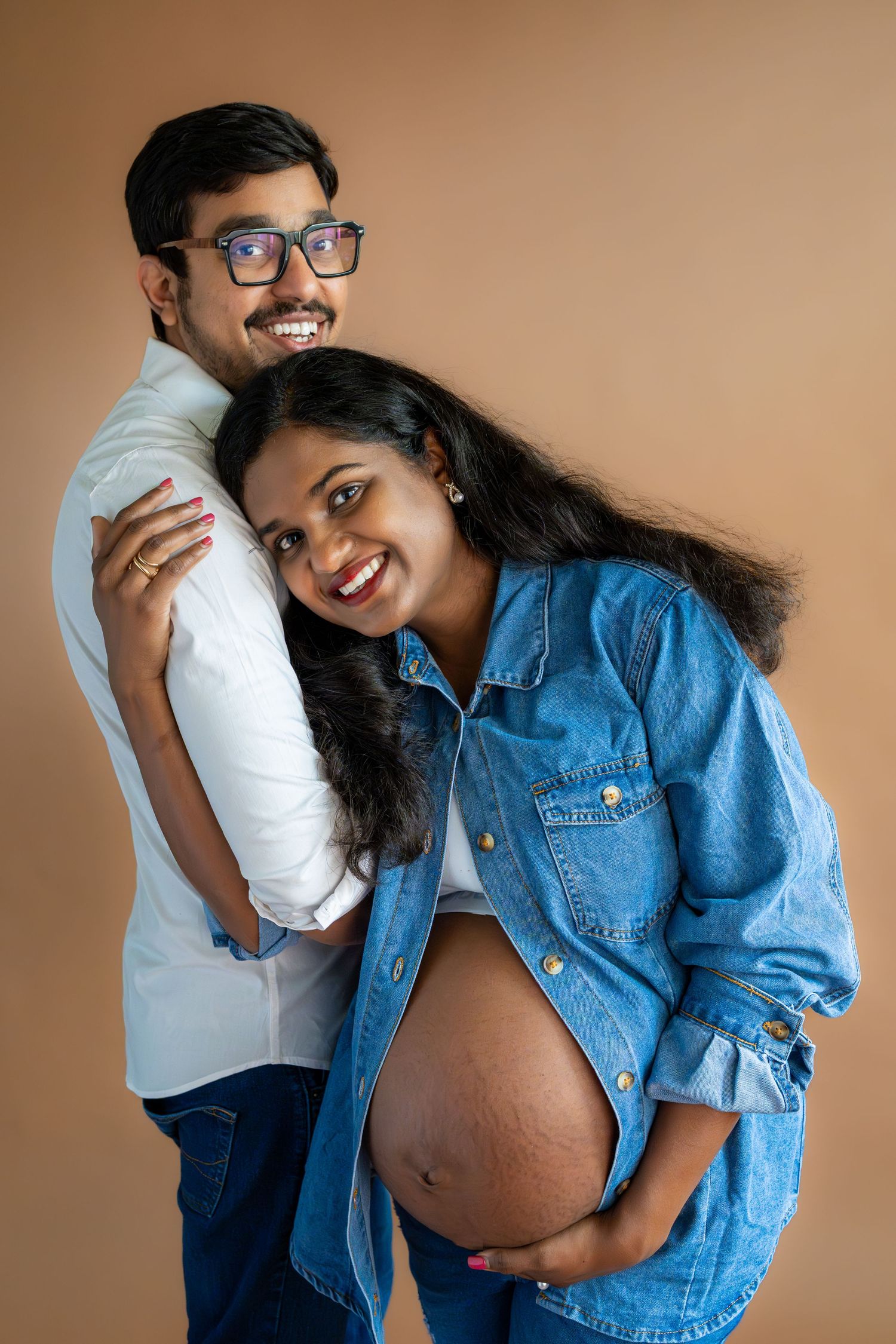 Happy Indian couple posing for maternity photo, pregnant woman leaning back against smiling man.