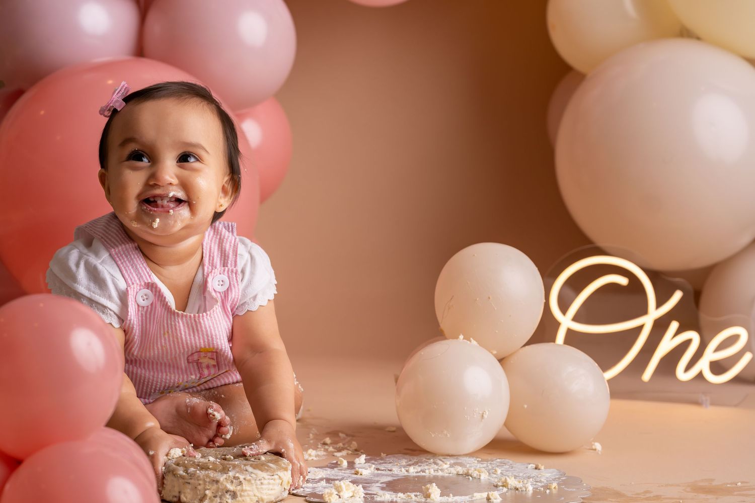 A first birthday celebration setup with pink and white balloons, cake, and decorative elements creating a festive atmosphere.