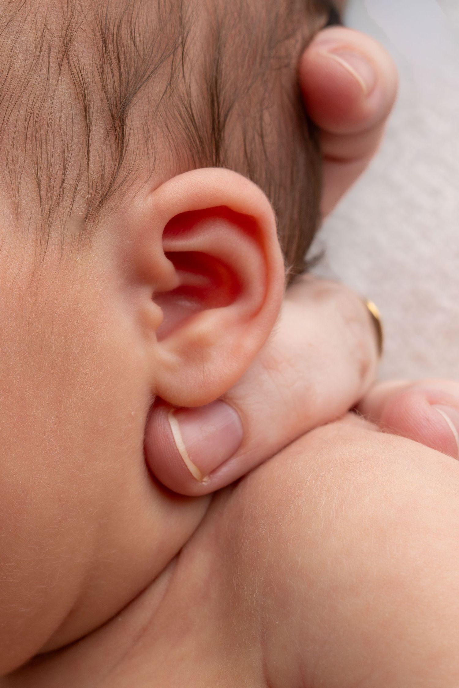Close-up of a newborn baby's ear with an adult's hand gently cradling the infant's head.