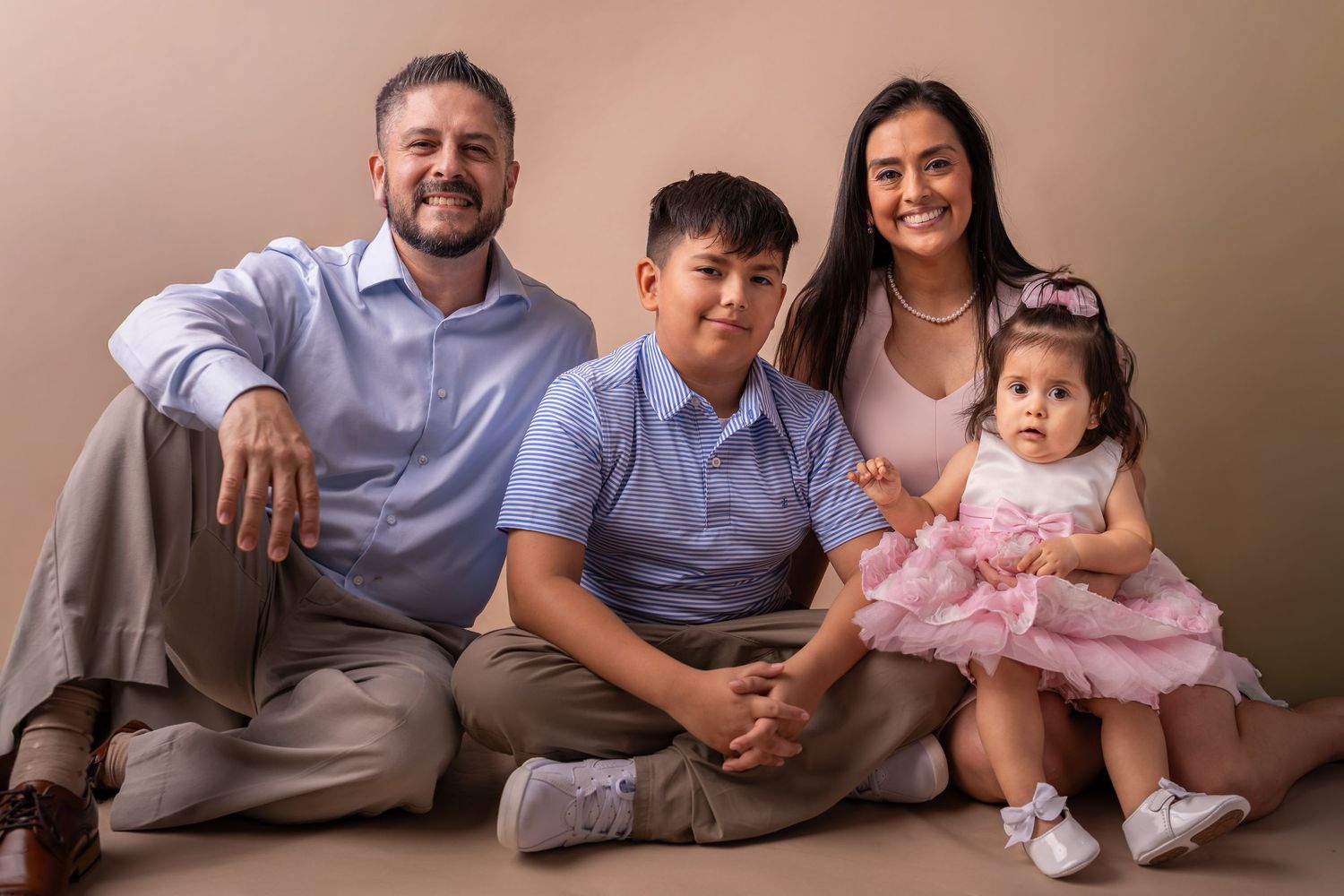 A family in coordinated gray and pink outfits poses together for a series of casual portrait photos on a beige backdrop.