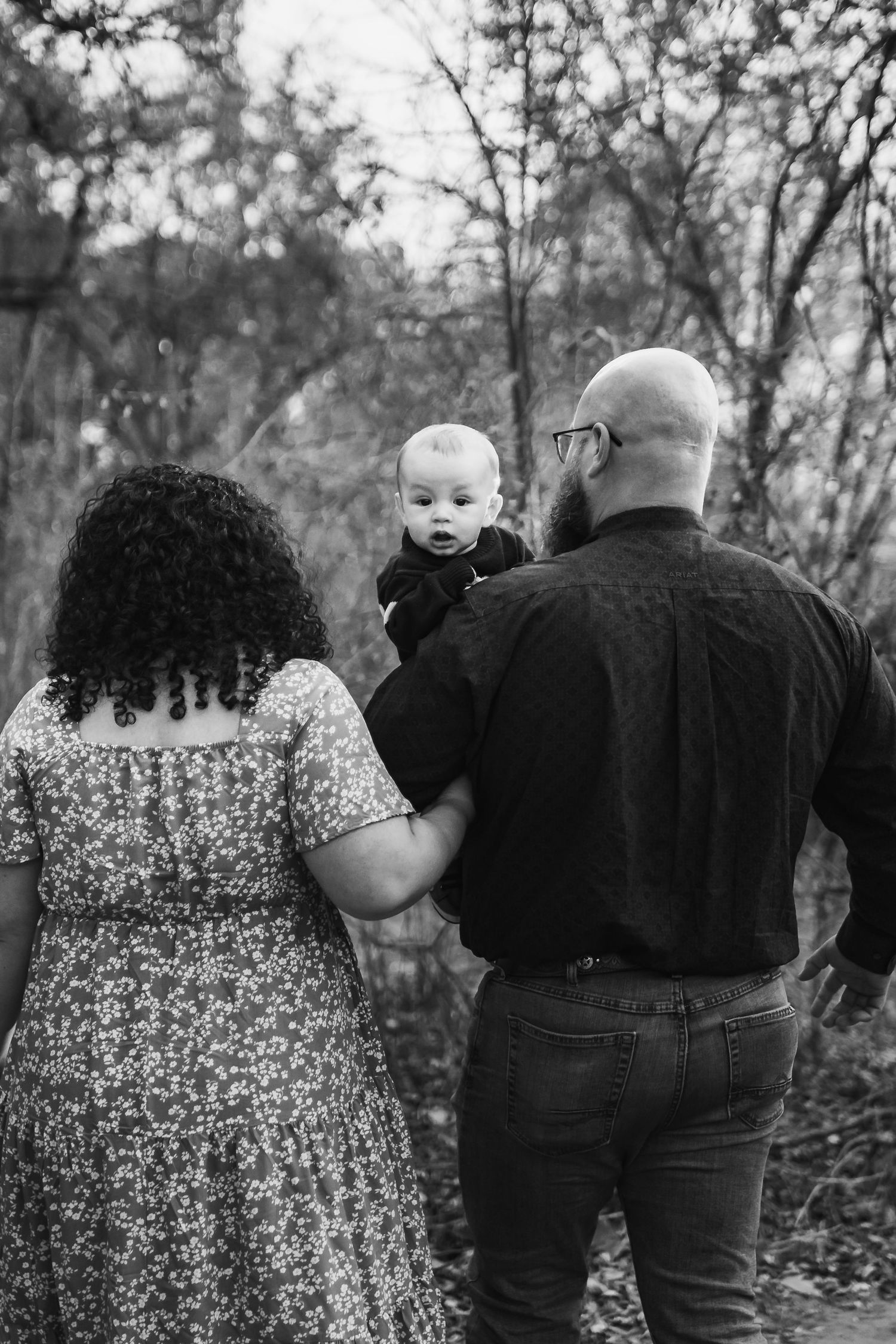 A black and white photo of a couple outdoors with their baby enjoying a peaceful moment in nature.