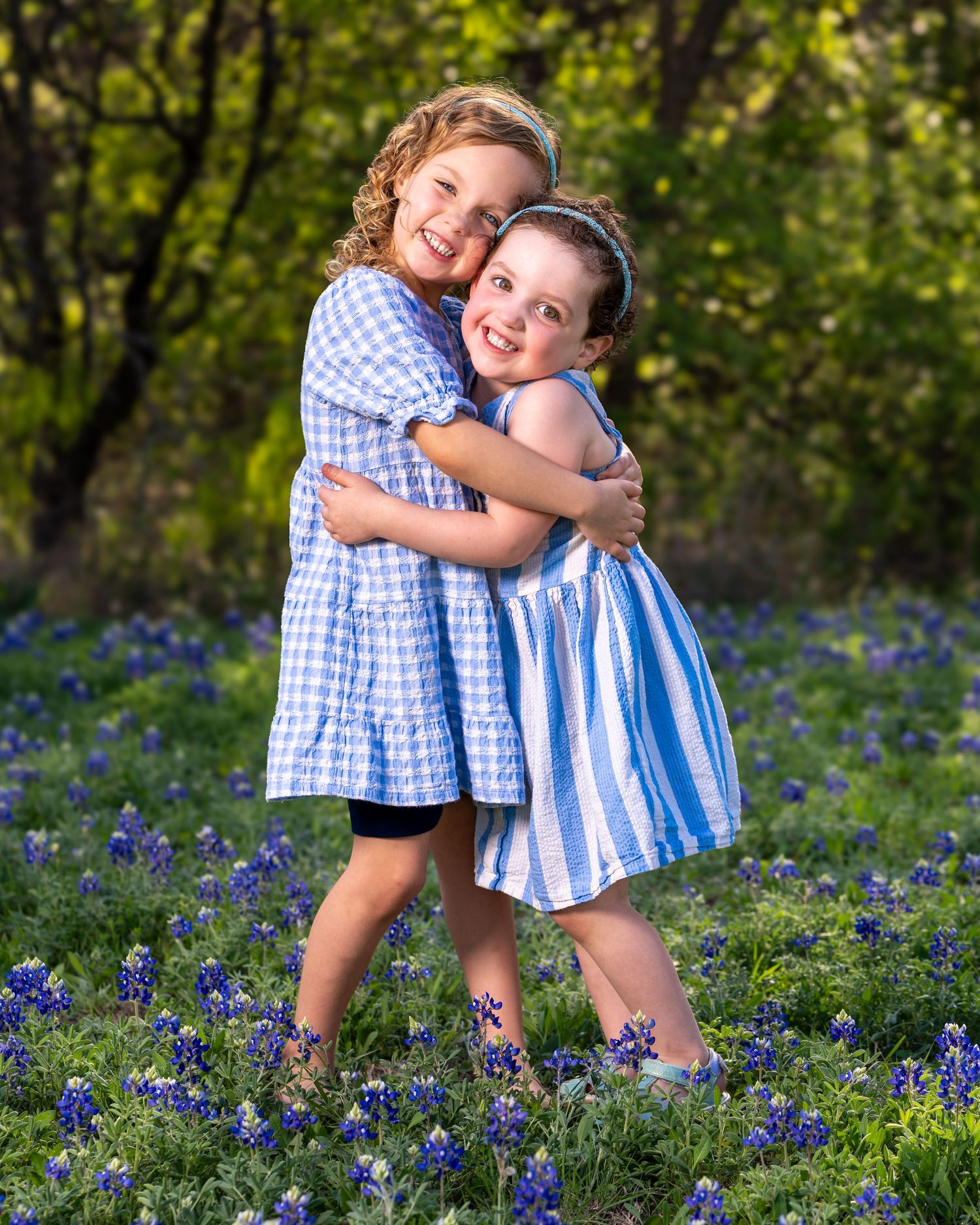 Two figures in coordinating blue and white outfits embrace while standing in a field of purple wildflowers.