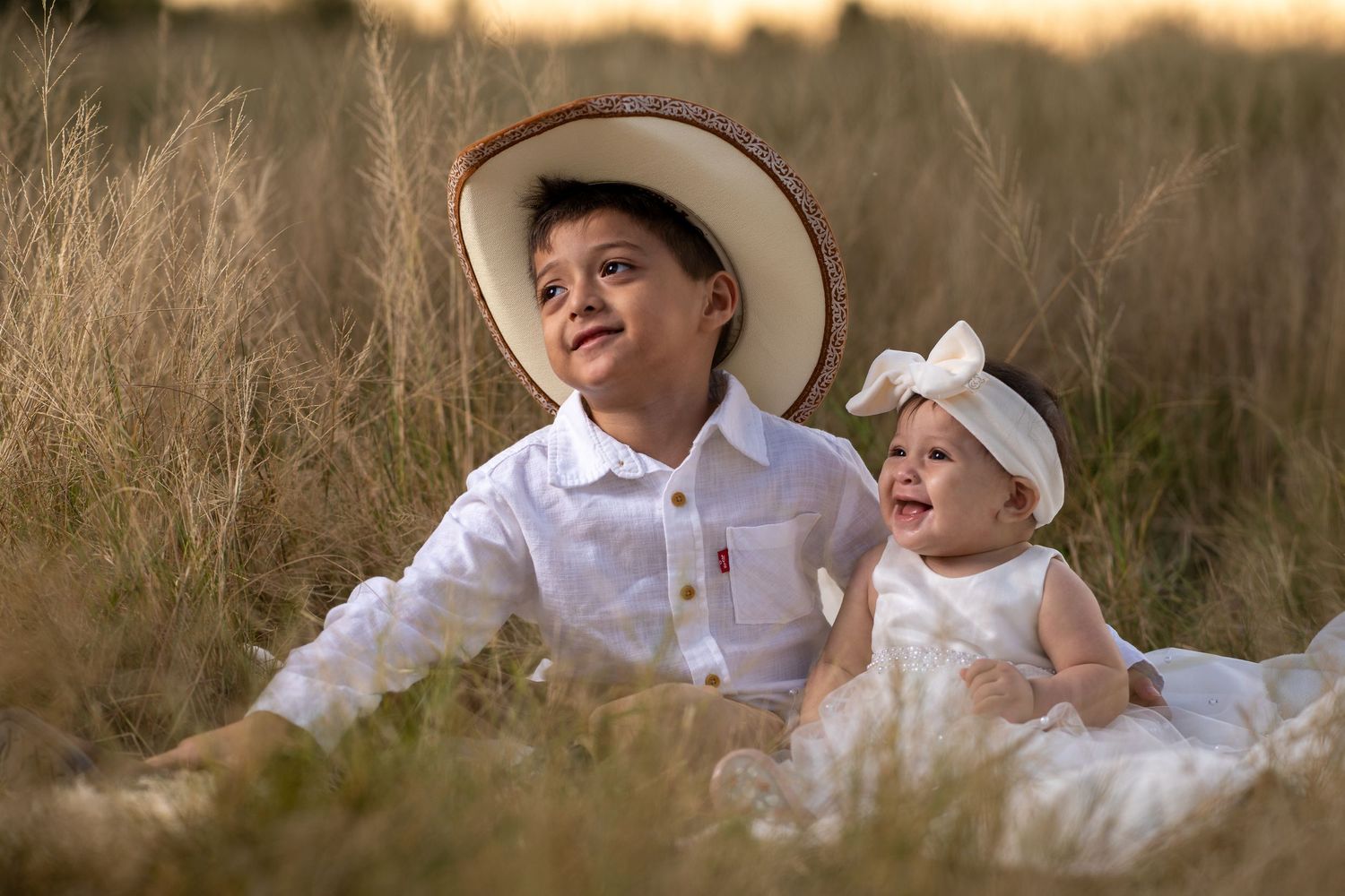 Two people in white clothing share a tender moment in a sunlit field during golden hour.