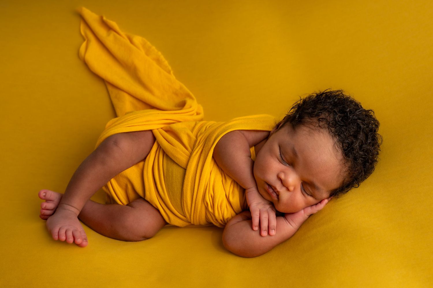 Newborn baby wrapped in yellow cloth sleeping peacefully on yellow background.