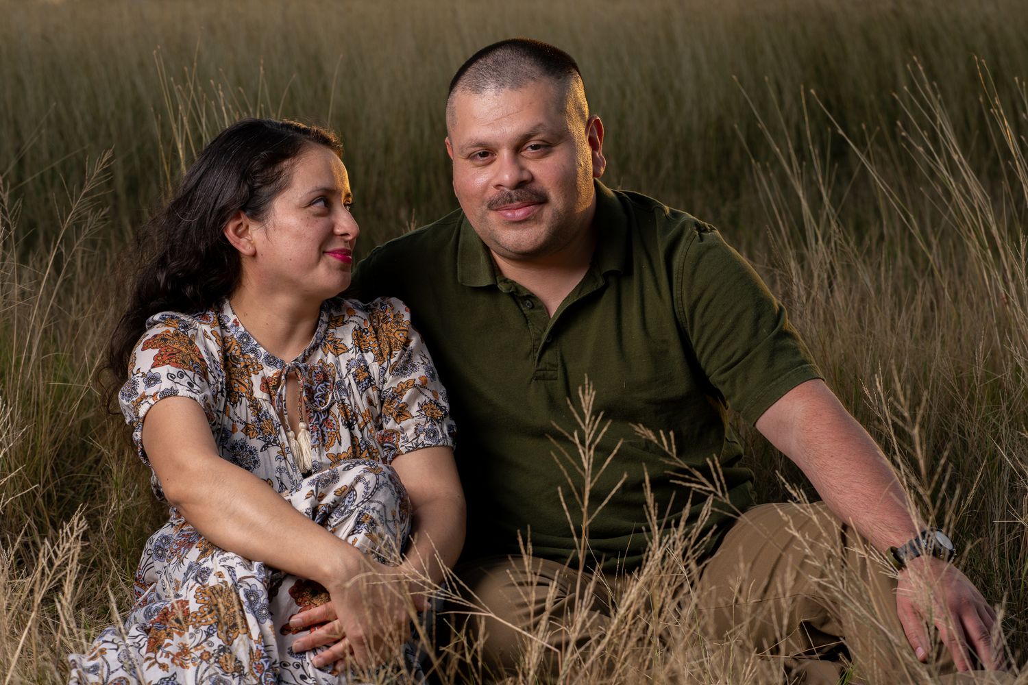 A couple lying in tall grass during a sunset photoshoot.
