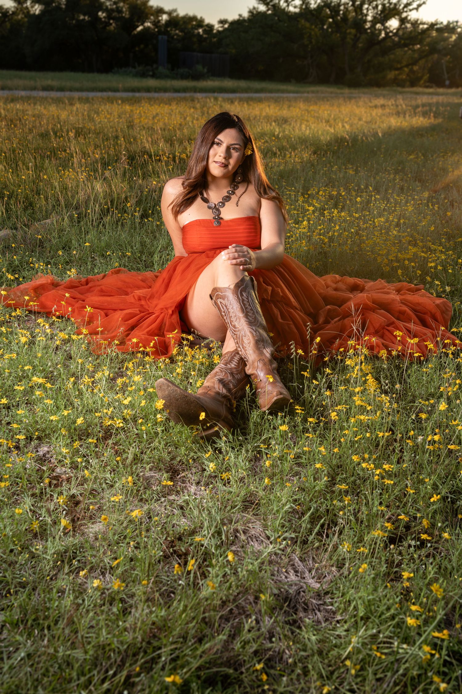 Woman in red tulle dress and cowboy boots sitting in wildflower field at golden hour.