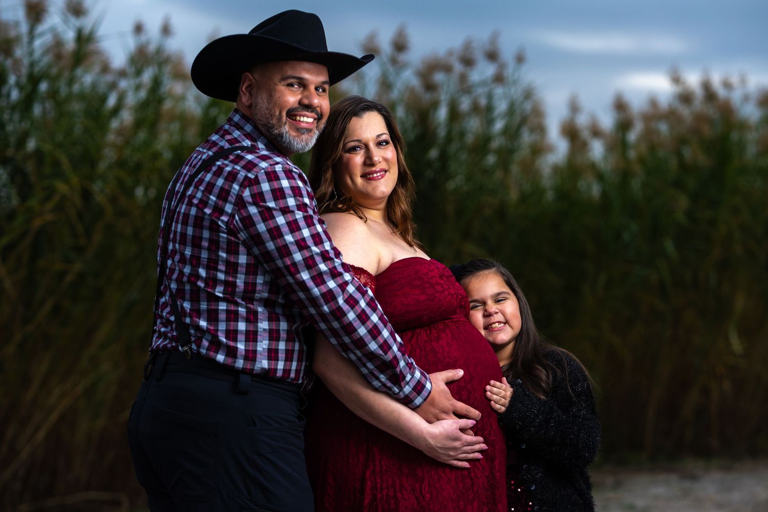 A family in western attire poses together outdoors against tall grass at sunset.
