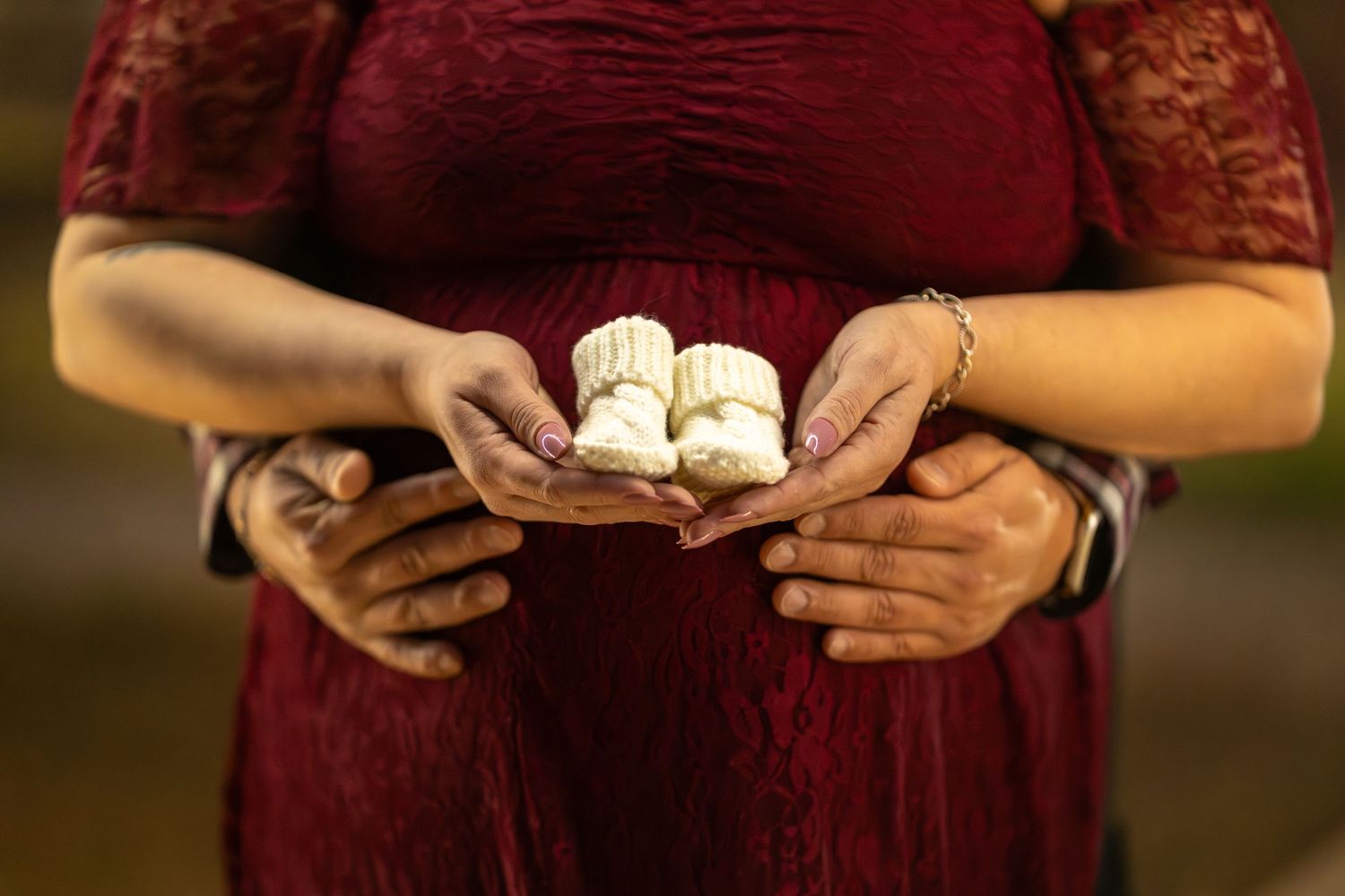 Close-up of parents holding white knitted baby booties during a winter maternity photoshoot at Lake Kyle Park, TX.
