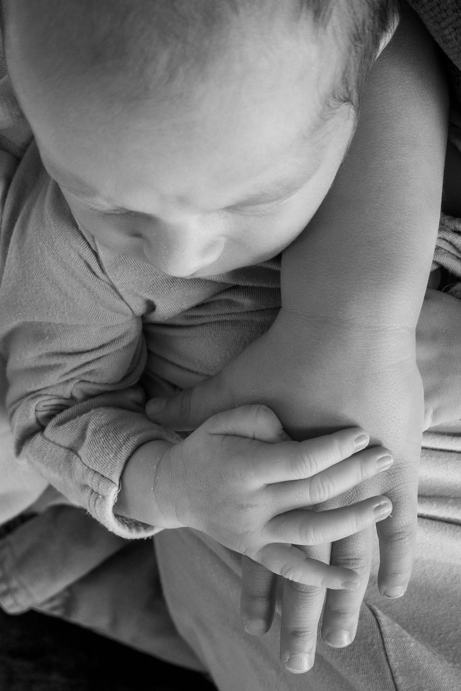 Black and white close-up of a baby resting with tiny hands folded together.