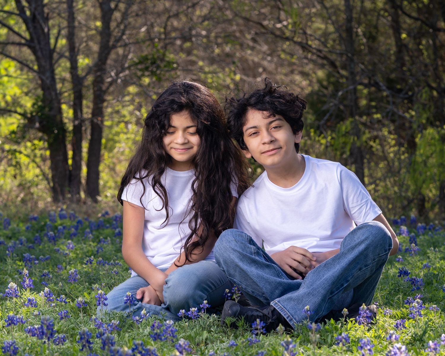 Two people sitting together in a field of blooming bluebonnets during springtime.