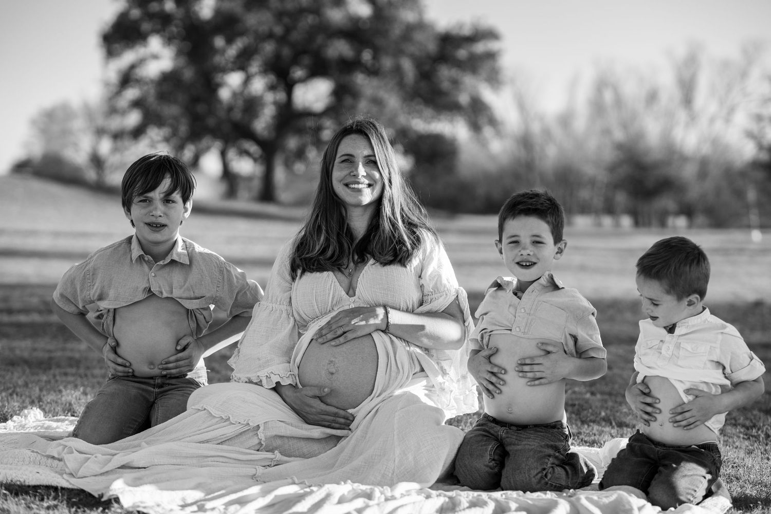 Black and white photo of a family sitting on a blanket outdoors holding pumpkins on an autumn day.
