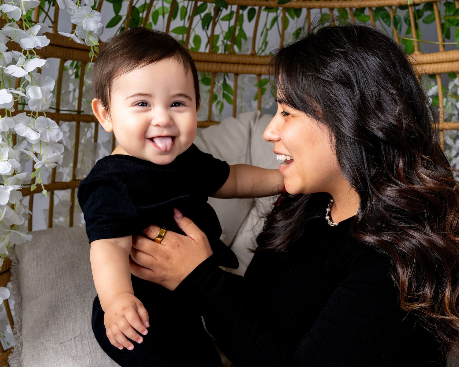 A joyful moment shared between a parent and baby wearing black, both laughing together against a light background.