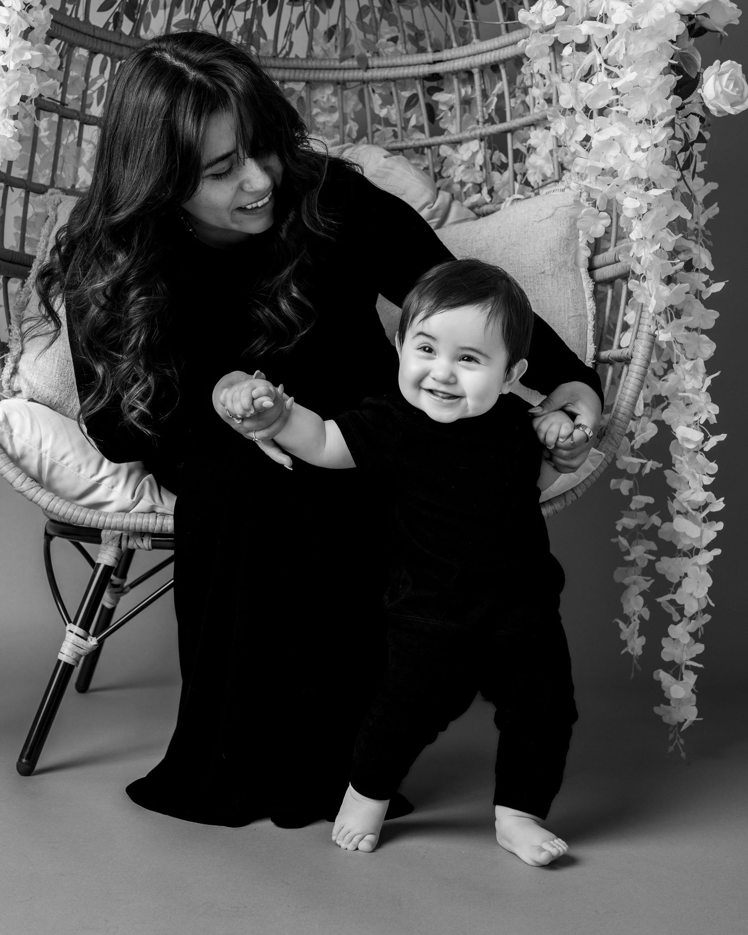 Black and white photo series showing tender moments between parent and child playing together under hanging floral decor.