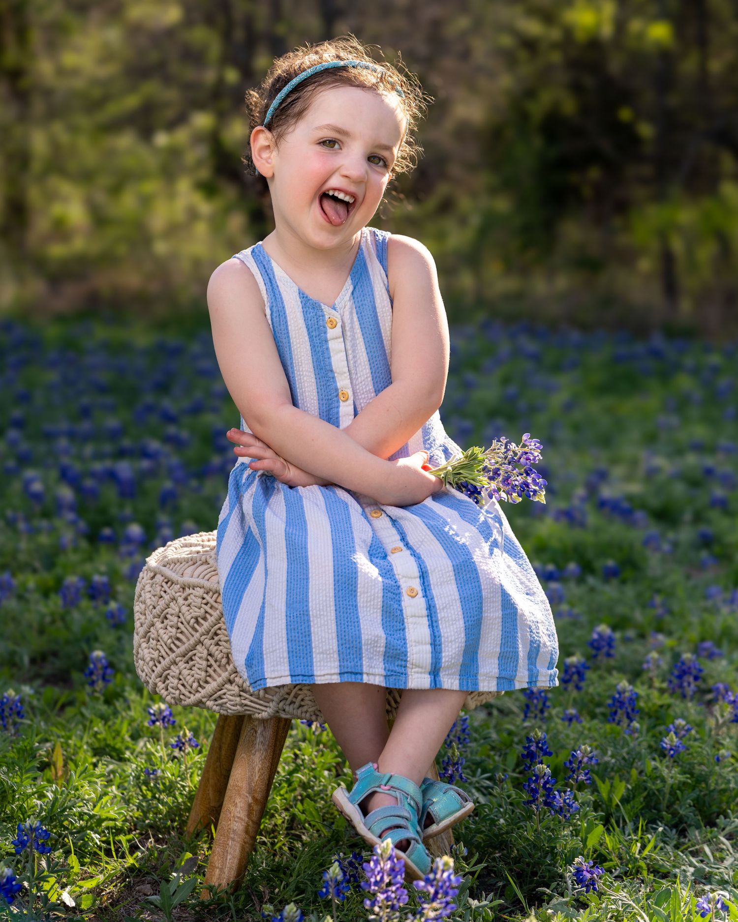 A joyful moment captured in a field of bluebonnets with a striped blue and white dress and rustic wooden stool.