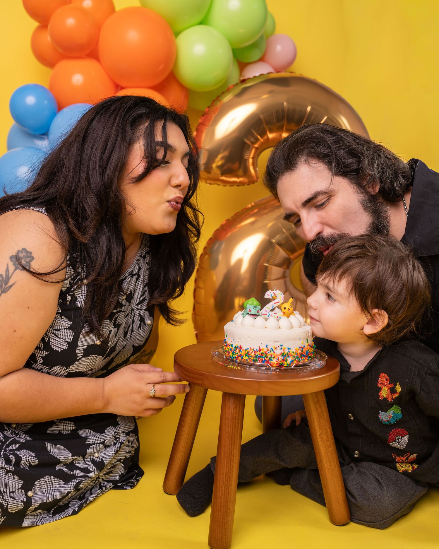 Family poses together with colorful balloons against yellow backdrop in playful studio photoshoot.