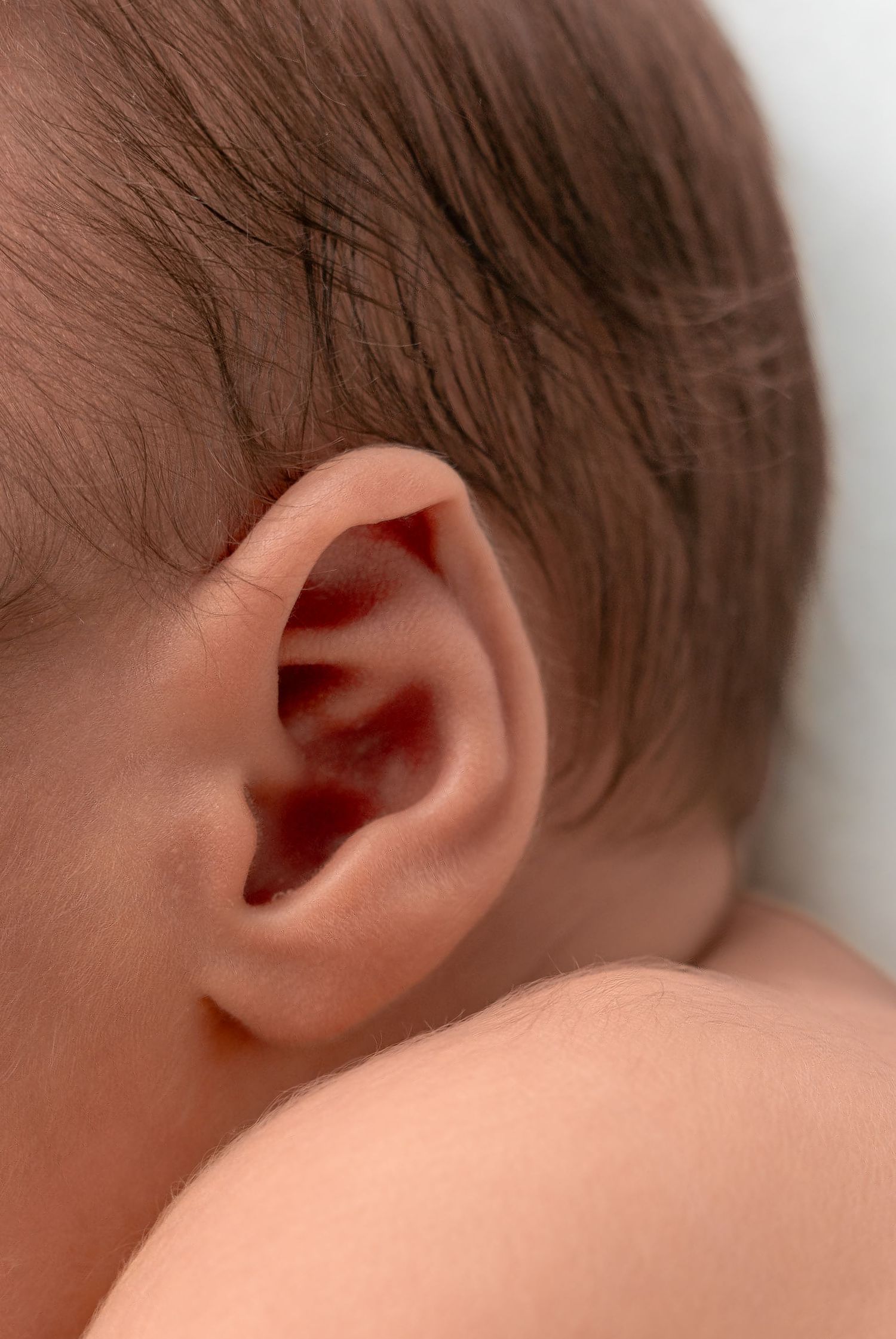 Close-up of a newborn baby's ear with fine brown hair visible.