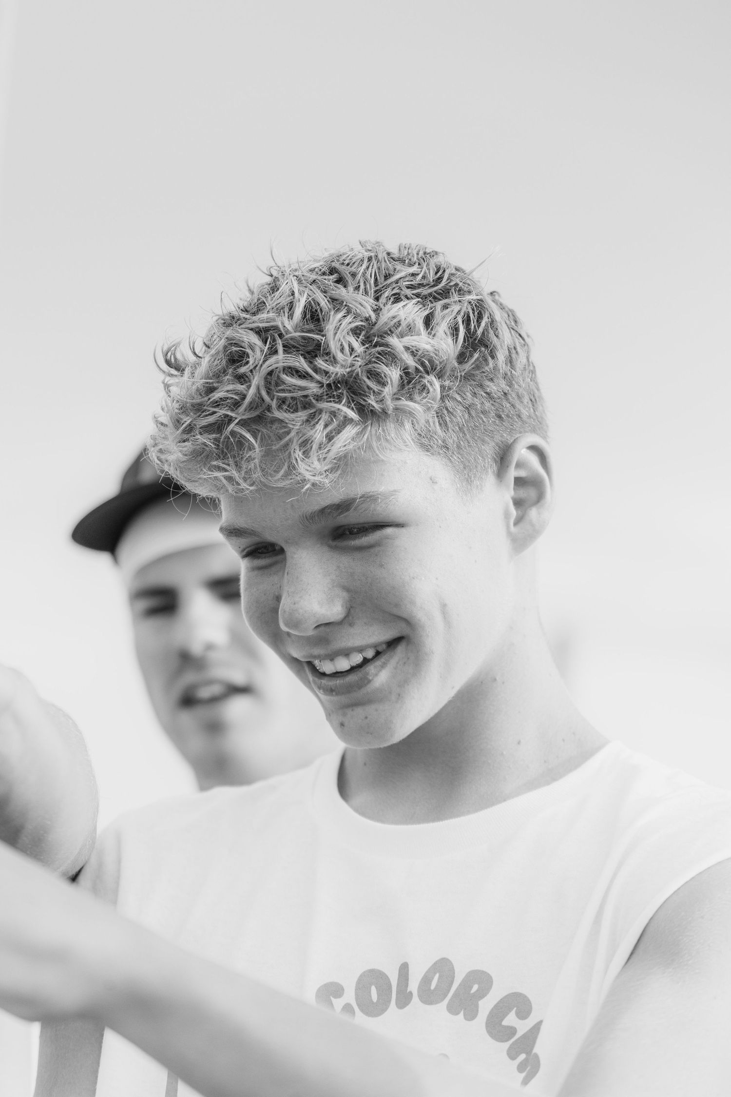 Black and white portrait of a smiling teenage boy with curly hair wearing a Color Chaos t-shirt.
