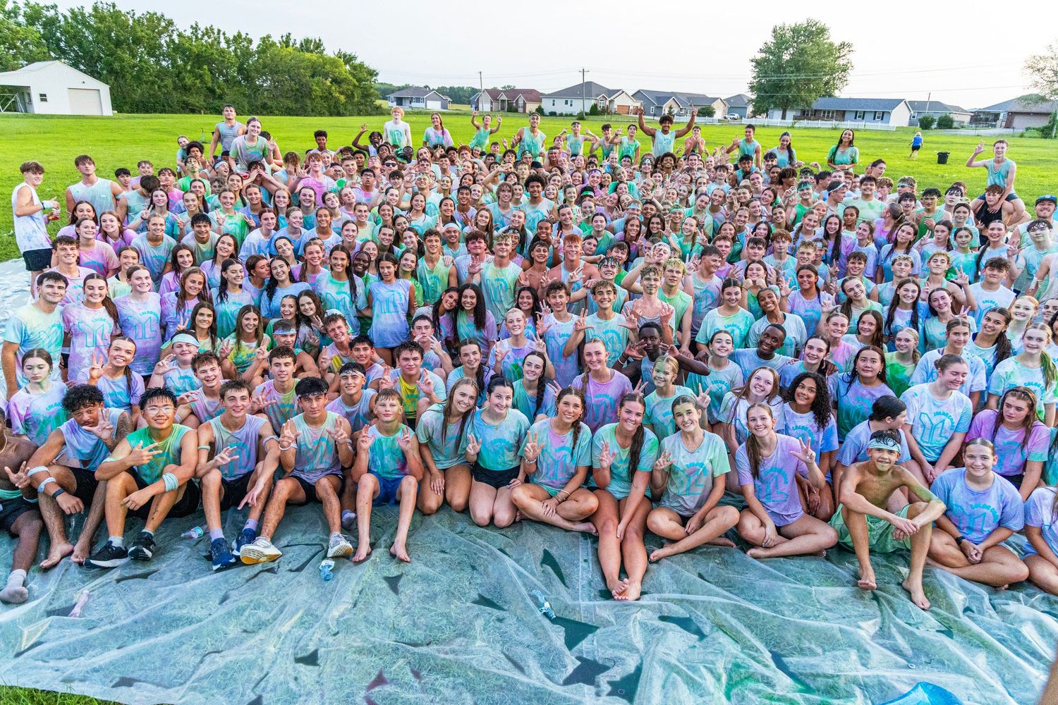 Large group of smiling students in colorful tie-dye shirts posing together on a green lawn.