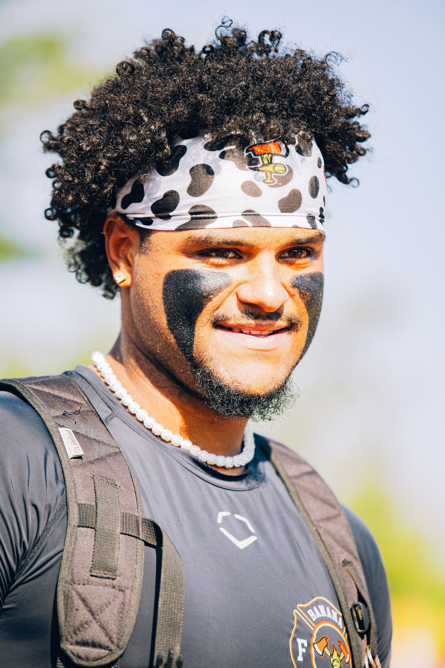 A smiling football player with an afro wearing a cow-print headband and eye black.
