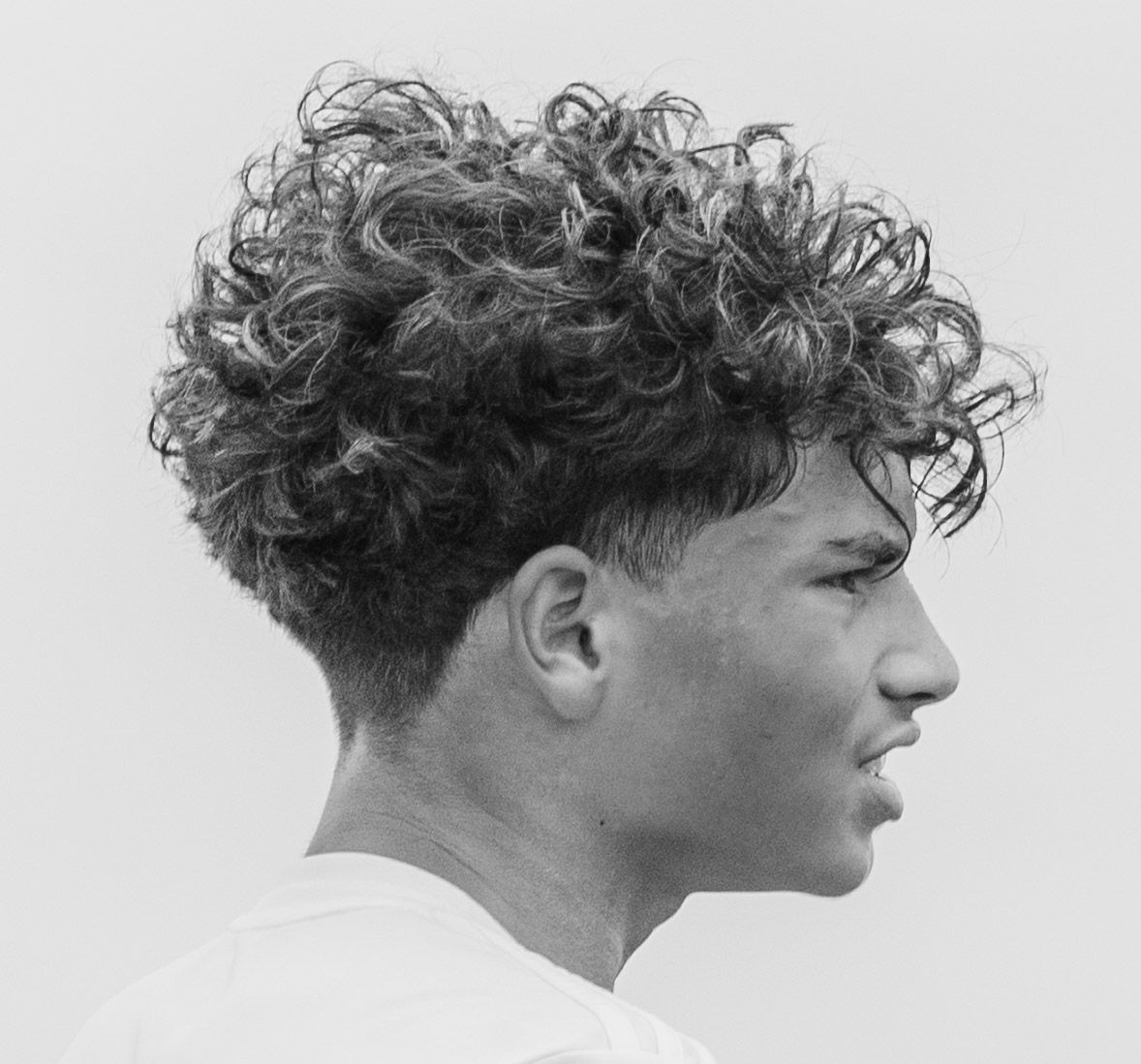 Side profile of a young man with curly hair and a fade haircut in black and white.