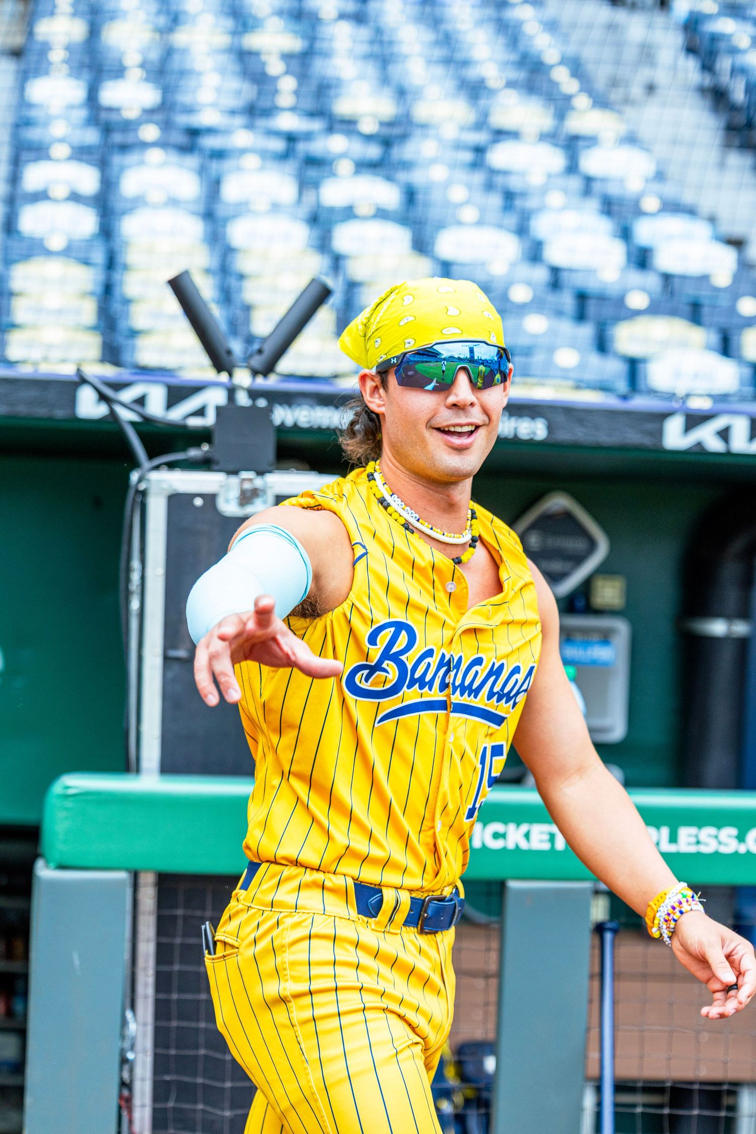 A baseball player in a yellow Savannah Bananas uniform points at the camera in a stadium.