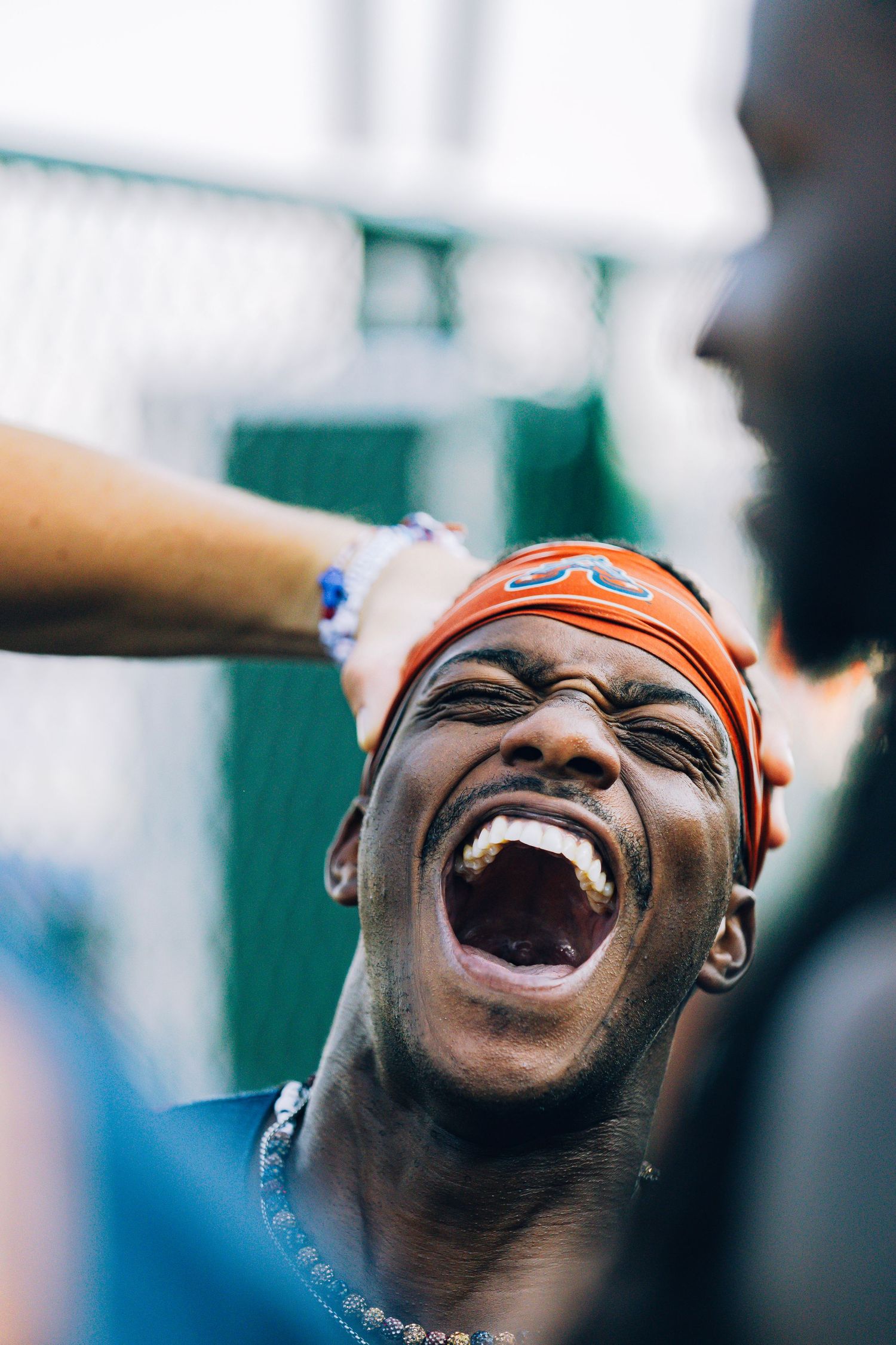 An excited athlete laughing with mouth wide open wearing an orange bandana outdoors.