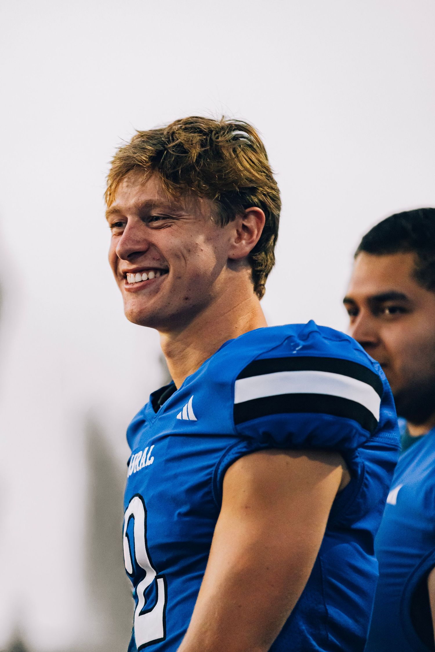 A smiling young football player in a blue Adidas jersey during an indoor game.