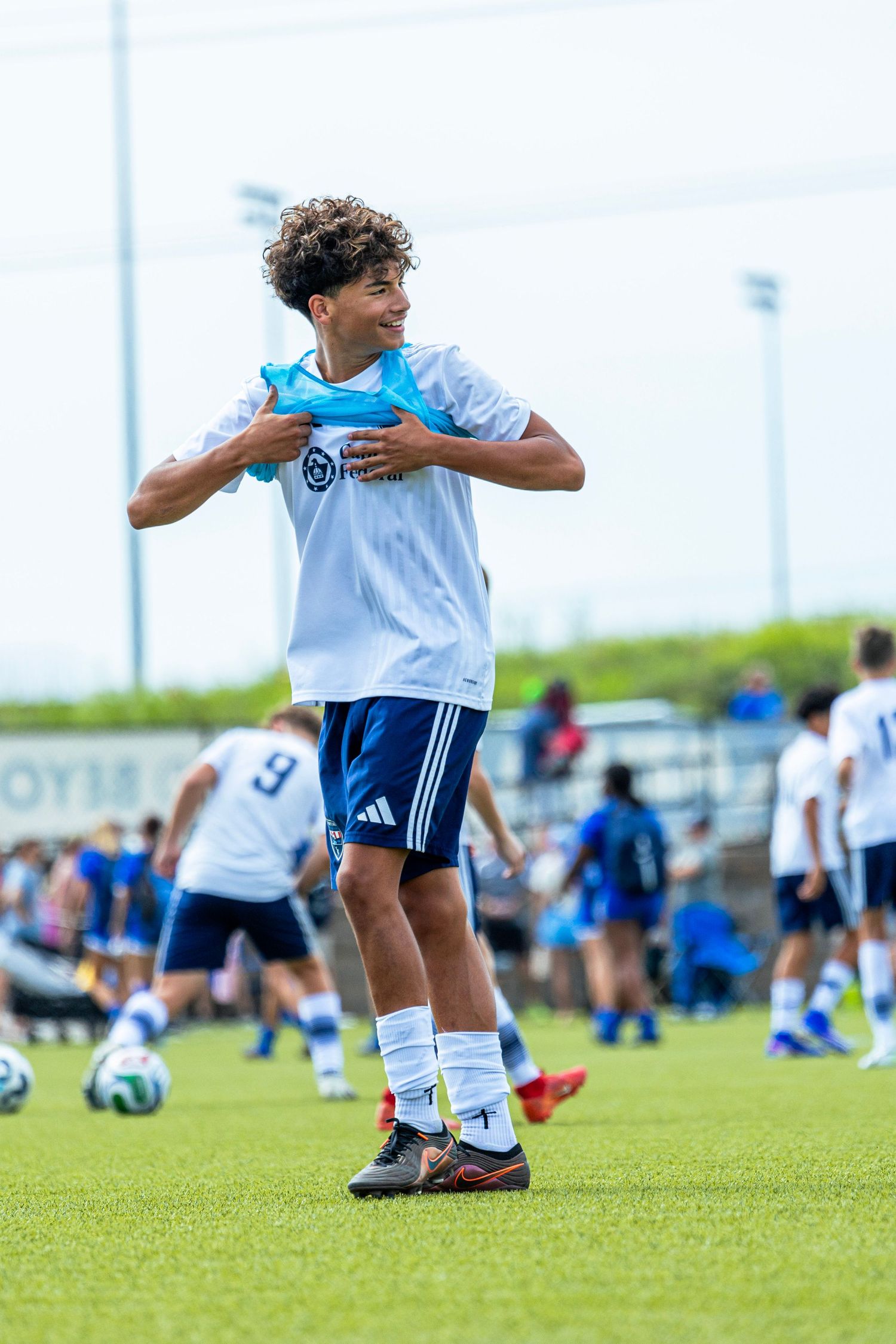 Young male soccer player smiling and adjusting his jersey during warm-ups on a soccer field.