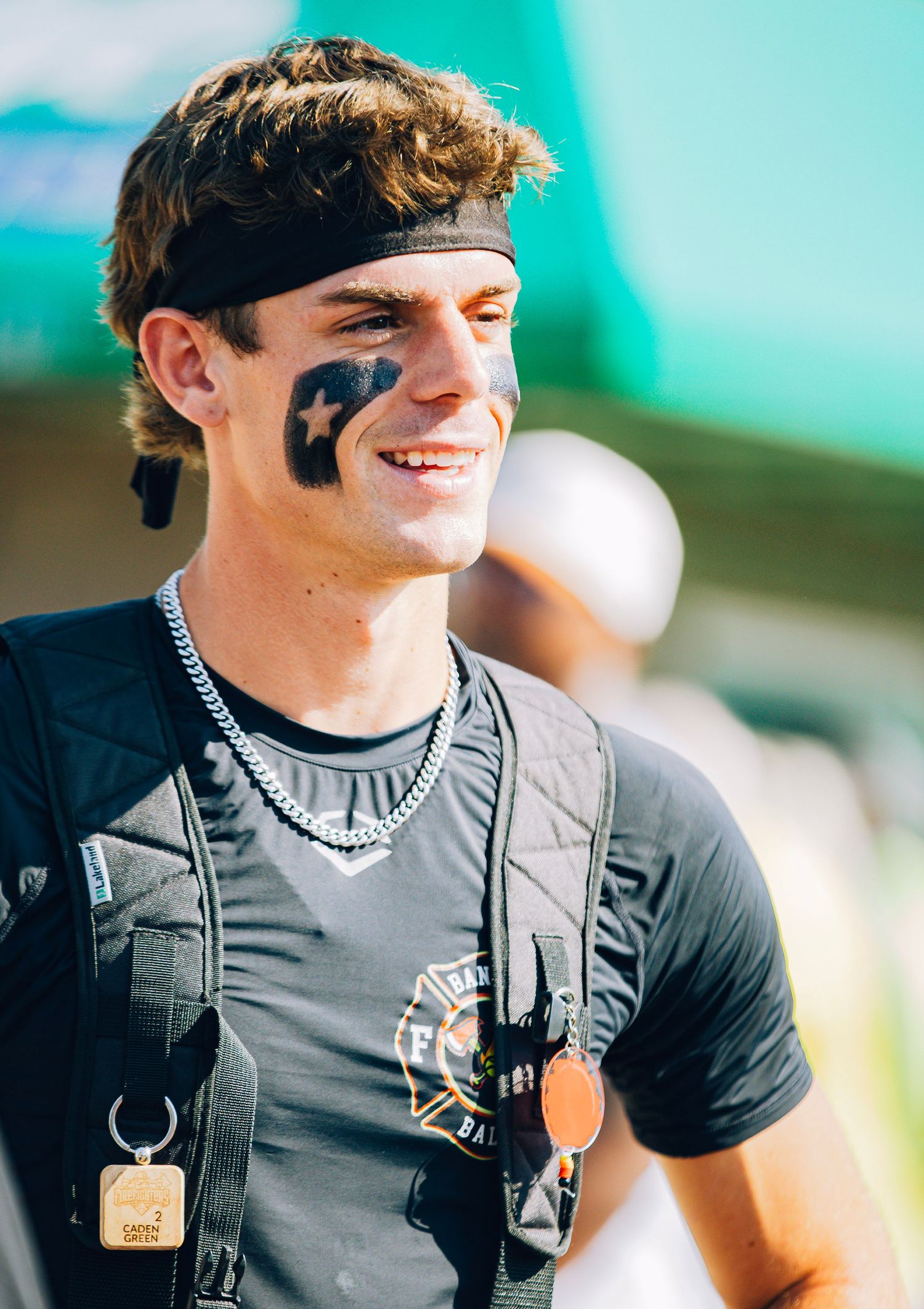 Young man with black face paint and headband smiling at an outdoor sports event.