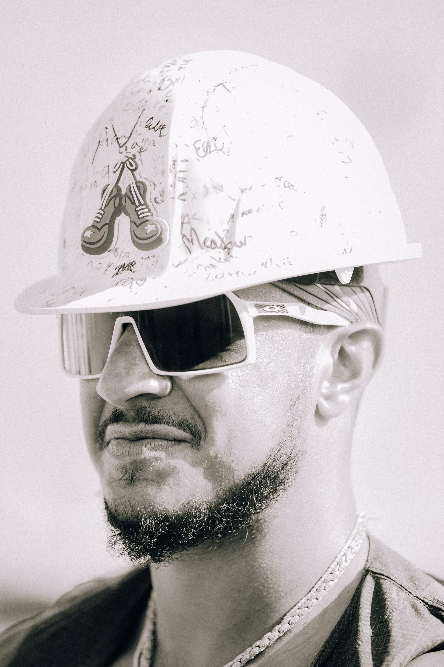 Black and white portrait of a man wearing a white hard hat and white sport sunglasses.