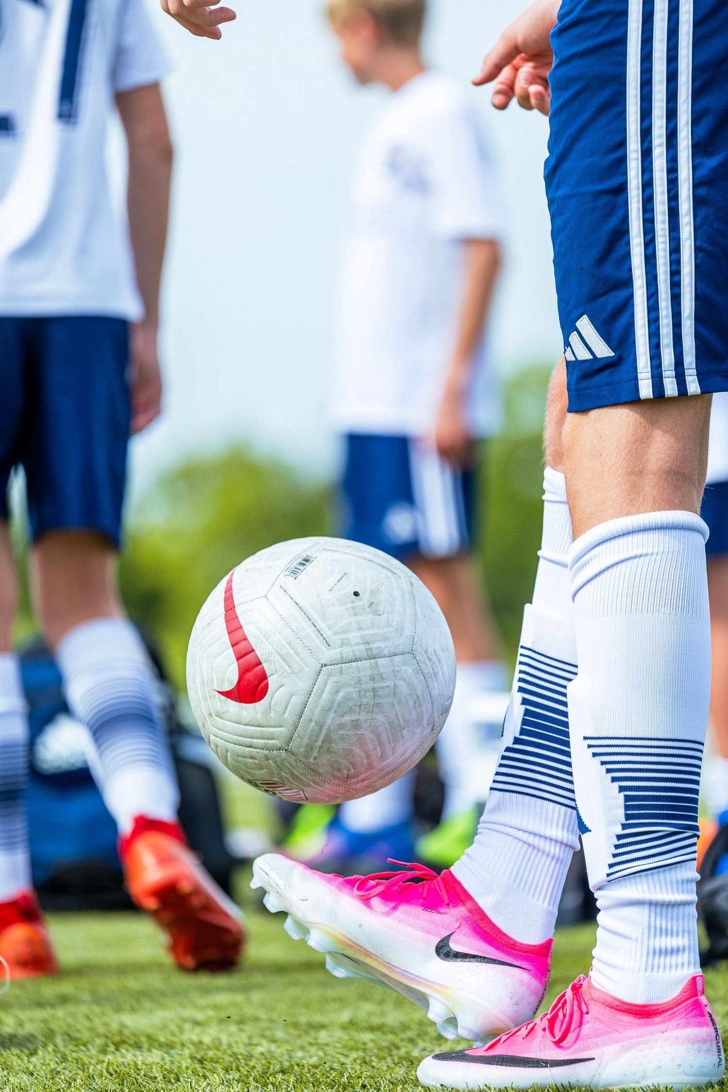 A soccer player in pink Nike cleats juggling a white Nike ball during a youth football match.