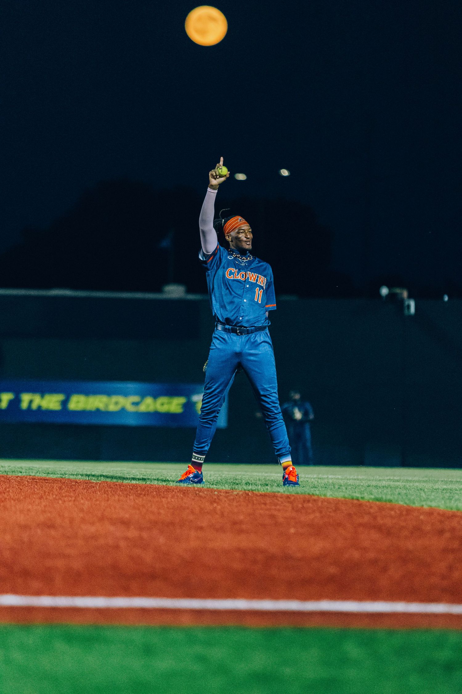 Baseball player in blue uniform tossing a ball under bright stadium lights at night.
