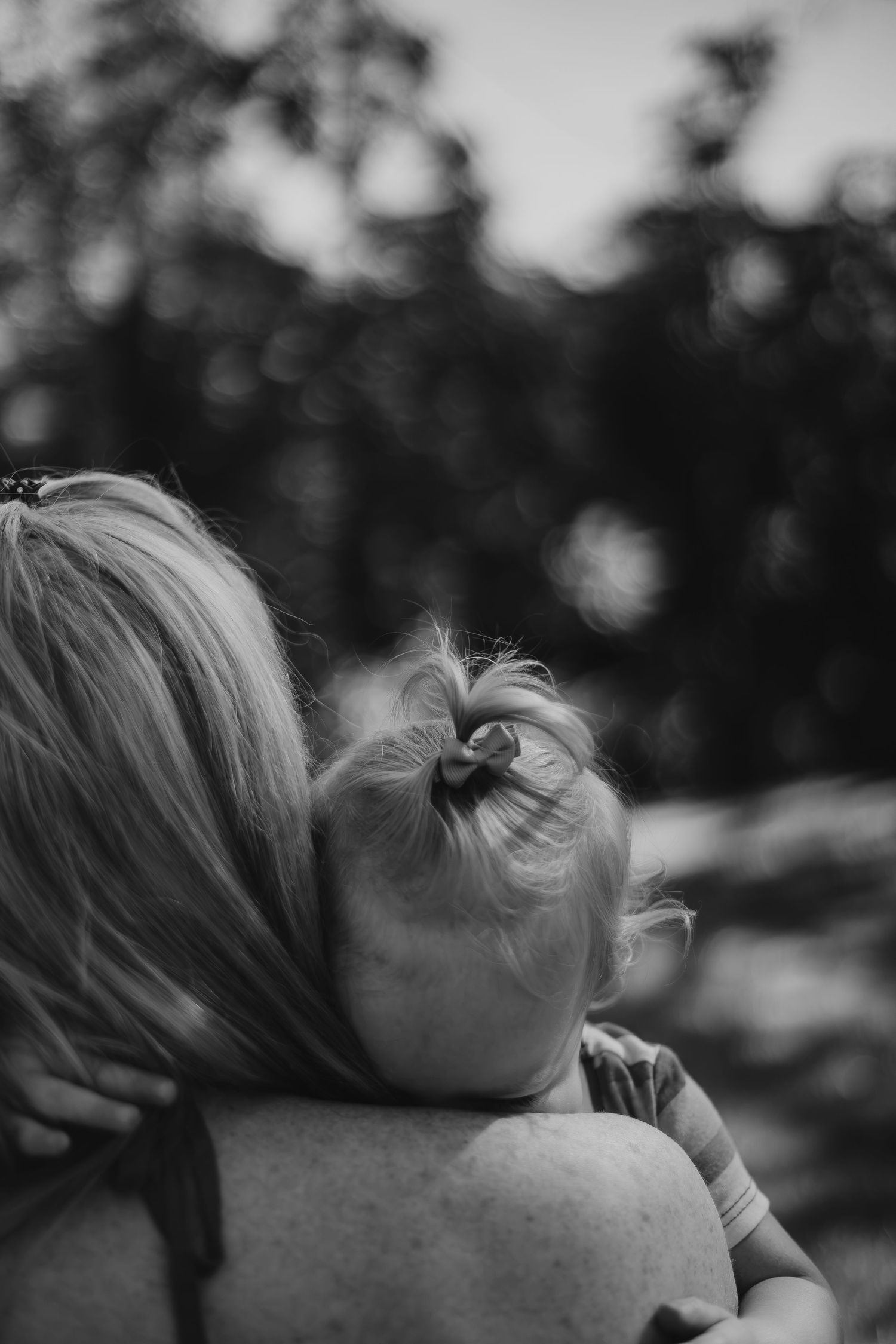 Black and white photo of a mother holding a baby resting its head on her shoulder outdoors.