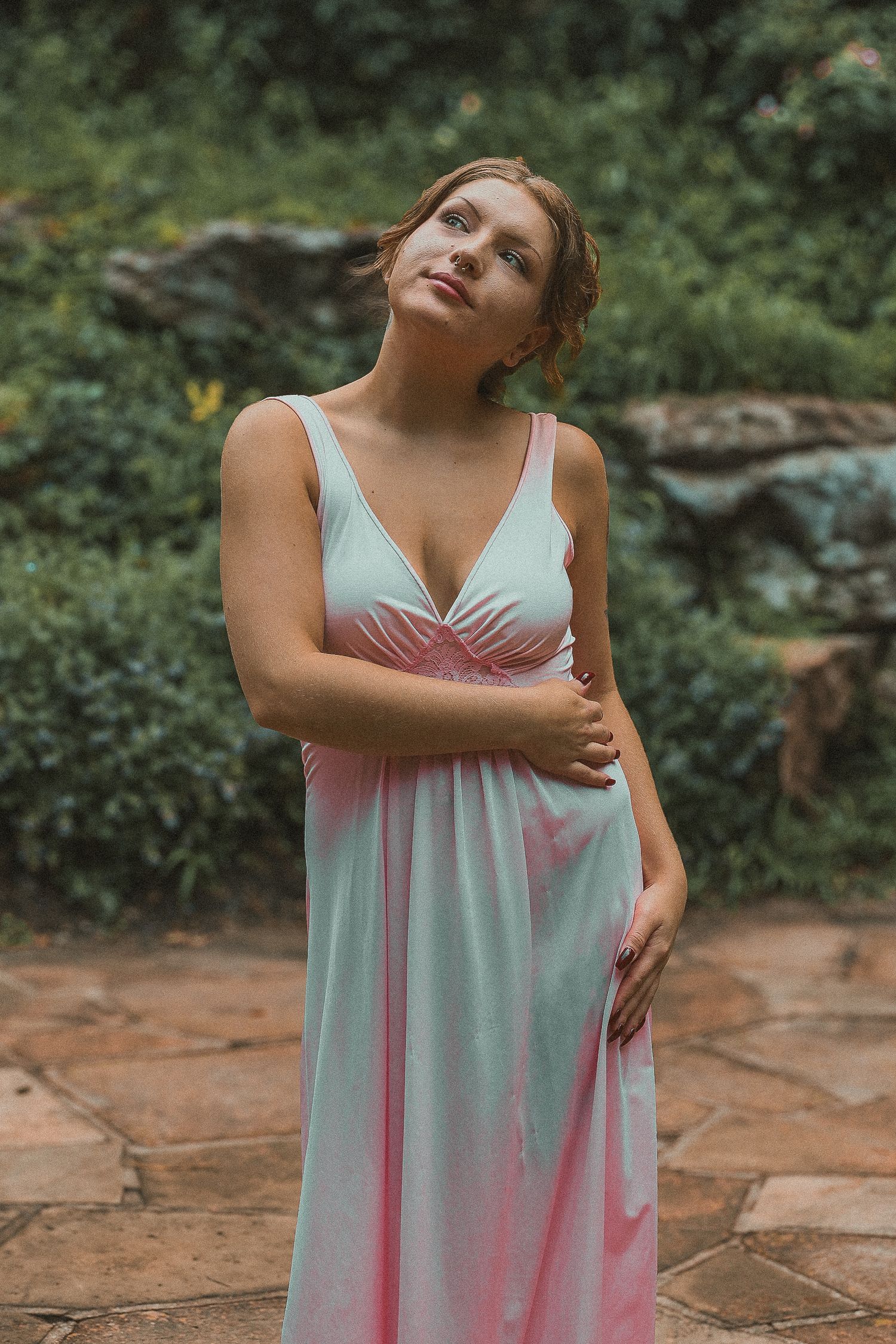 A woman in a flowing white sundress poses gracefully in a garden setting with stone pathways and greenery.