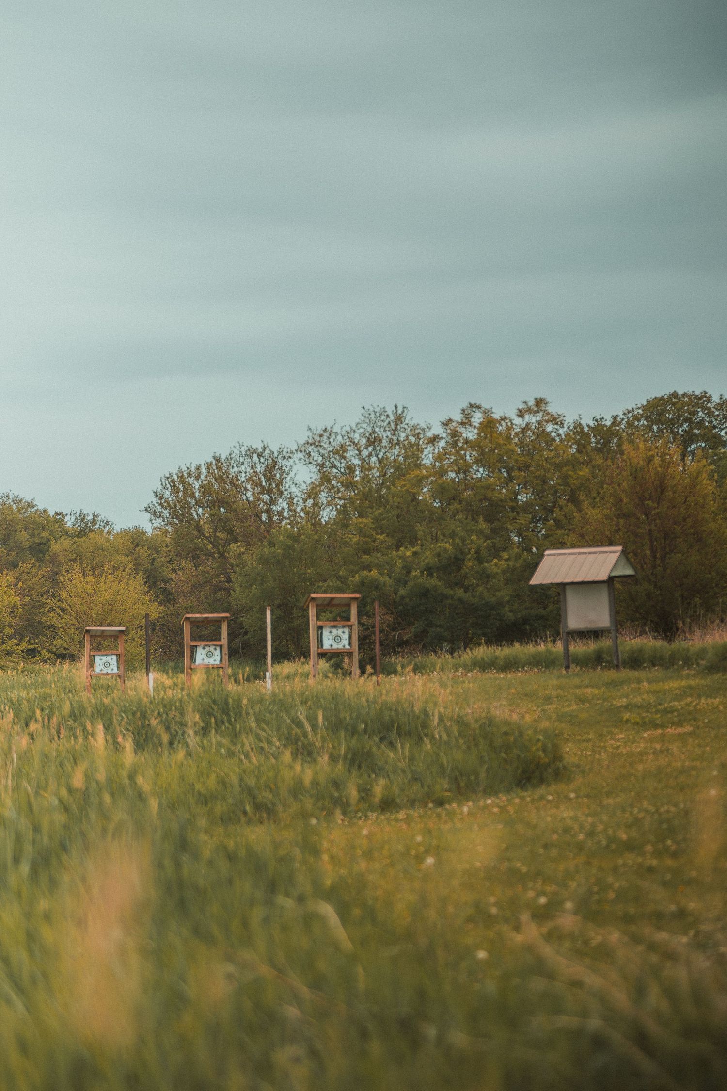 Wooden information boards and a small shelter stand in a green meadow with trees in the background under a cloudy sky.