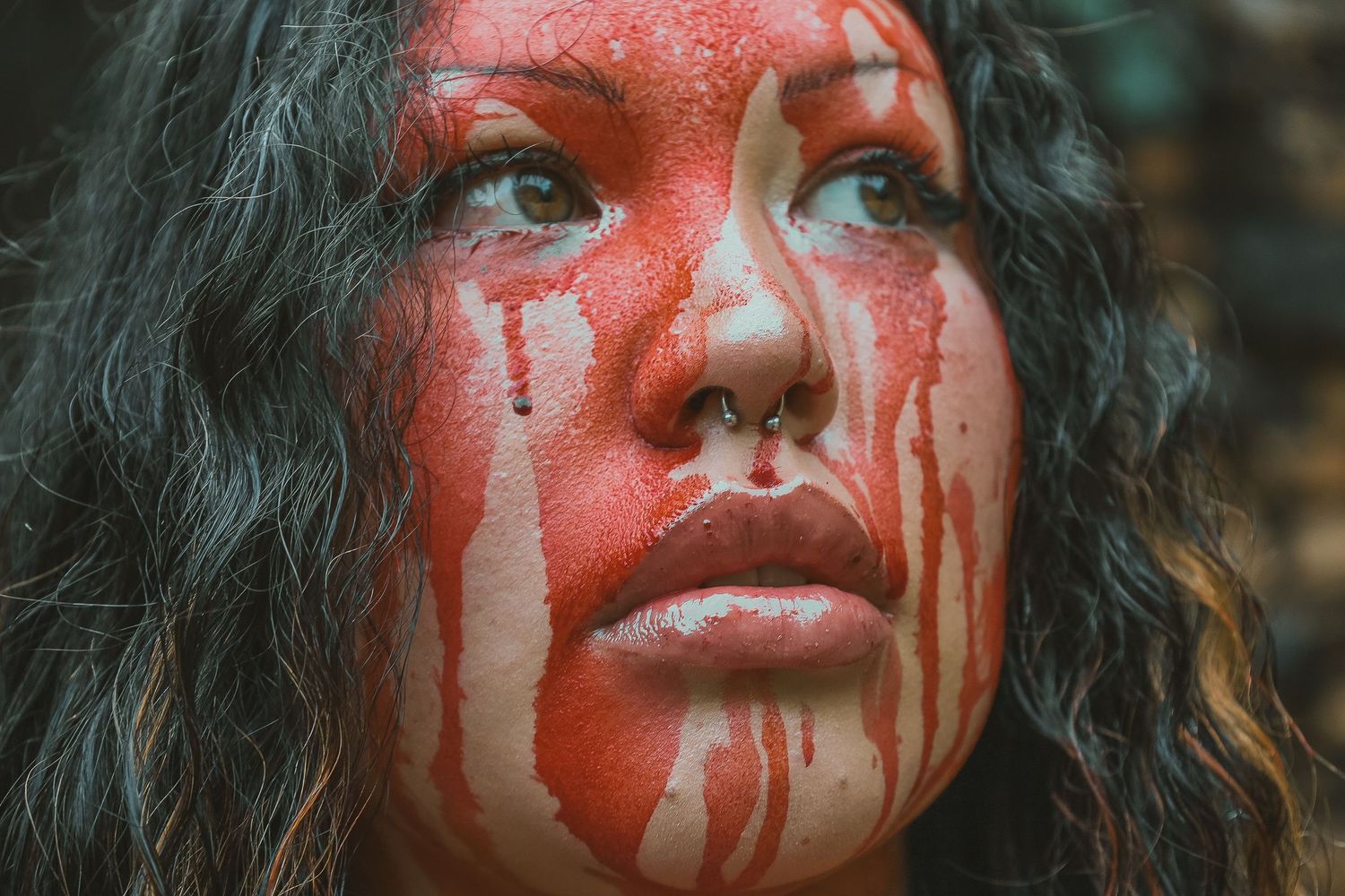 Woman with dramatic red paint dripping down her face in a dark, artistic horror-themed makeup look.