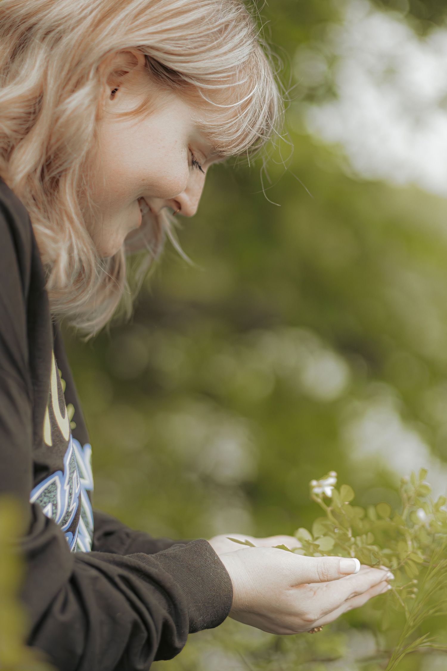 Smiling blonde girl gently cupping green plant leaves in her hands outdoors in nature.