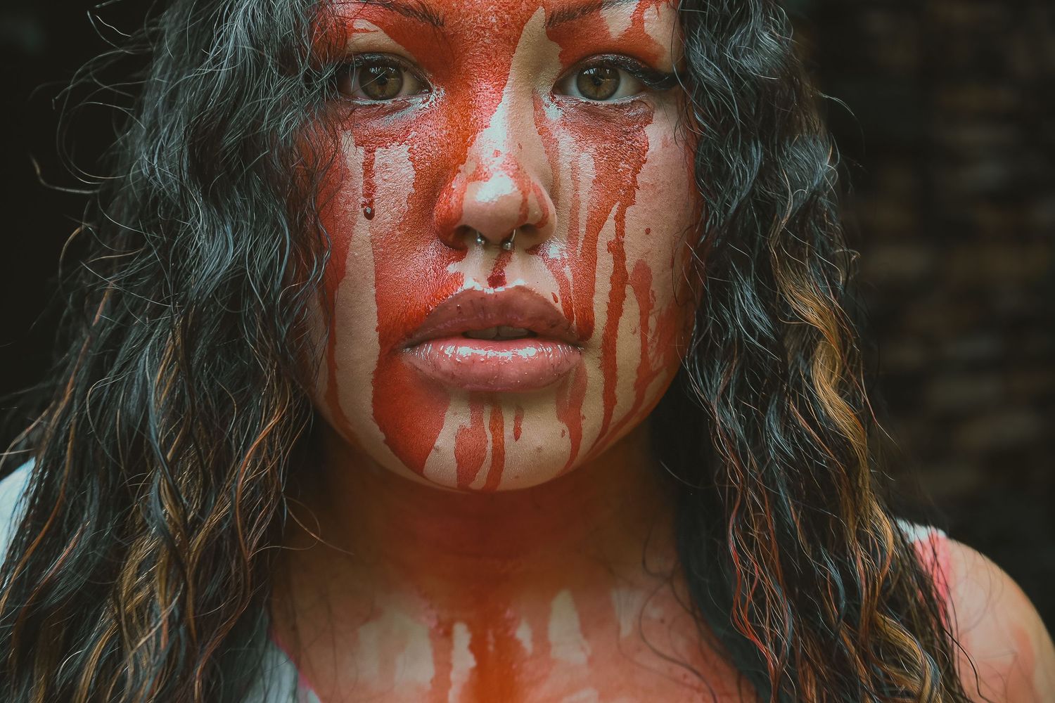 A person with dramatic blood drips down their face and tousled dark hair poses for an artistic portrait series.