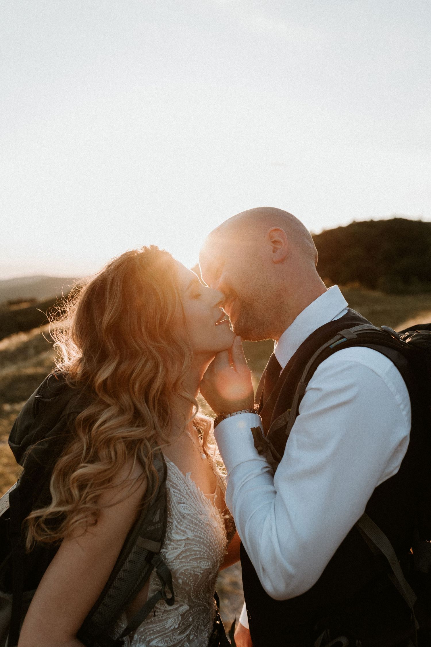 A romantic silhouette of a bride and groom kissing at sunset in an outdoor mountain setting.