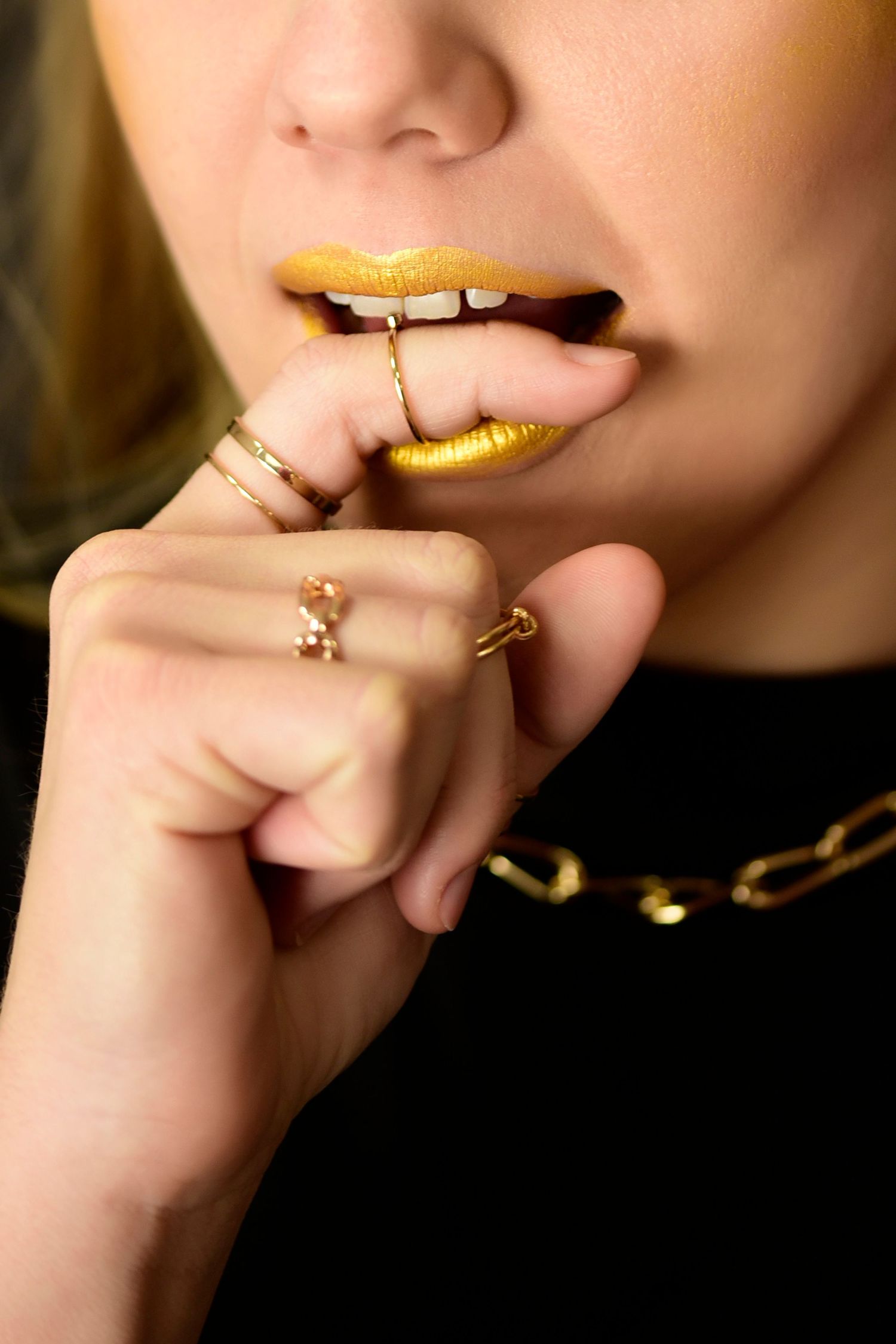 Artistic close-up of gold metallic lipstick and jewelry on model's lips and hands.
