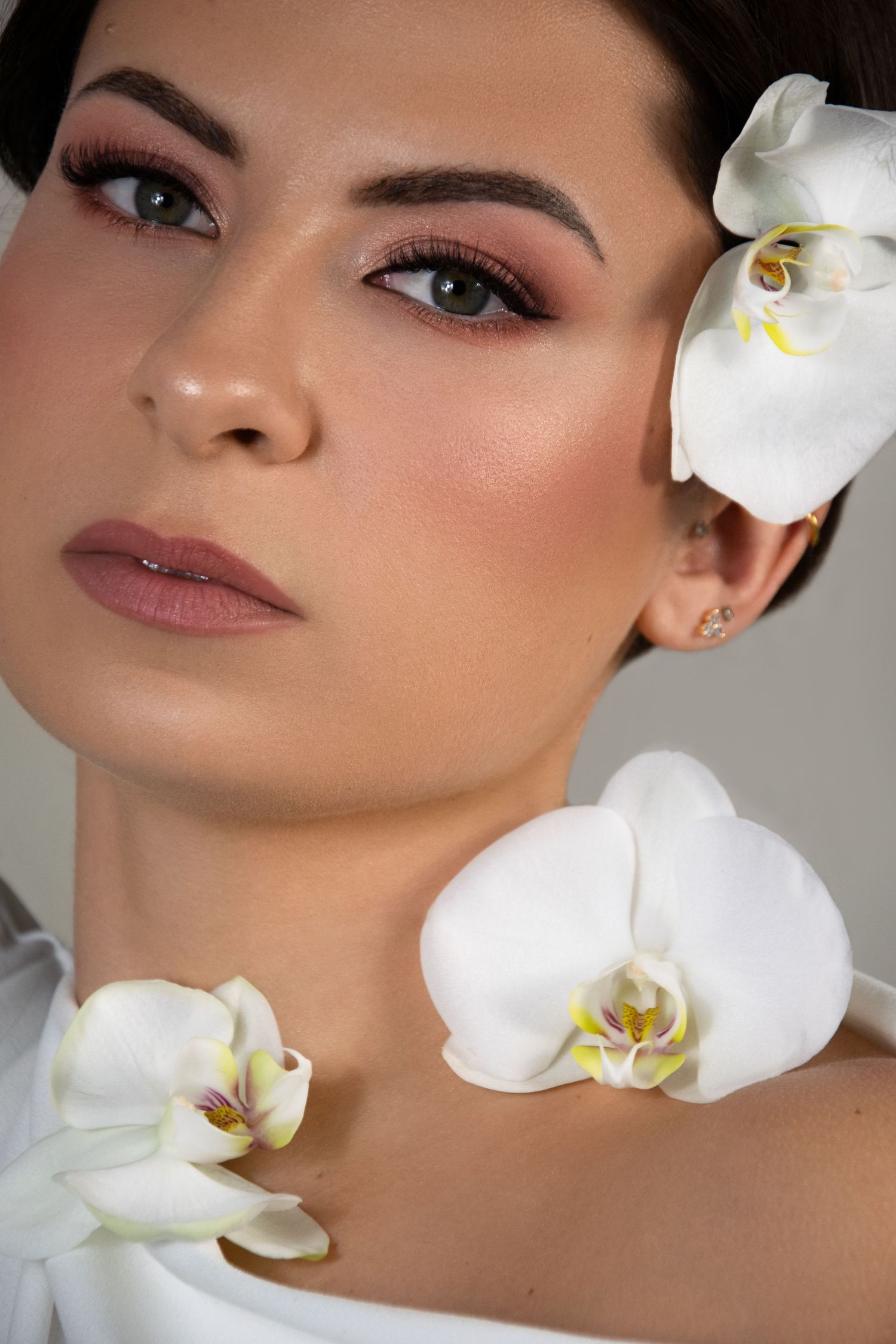 A woman with elegant makeup and white orchid flowers in her hair poses gracefully for a beauty portrait.