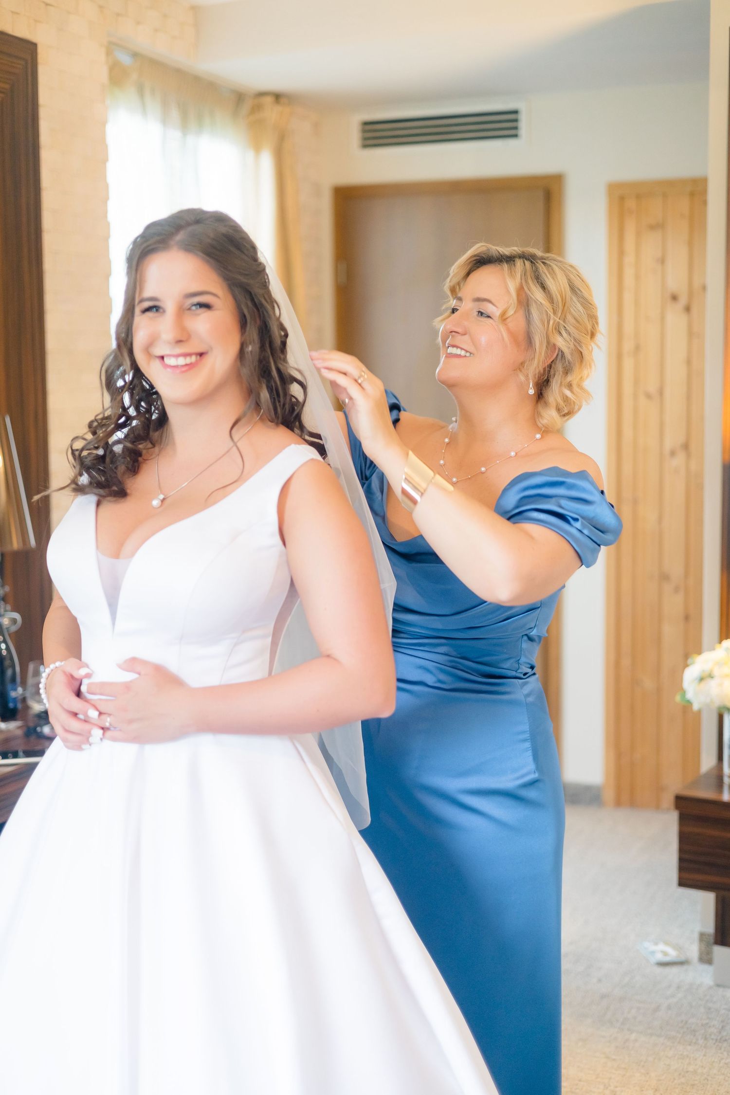 A bride wearing a white dress shares joyful moments with bridesmaids in royal blue dresses during wedding preparations.