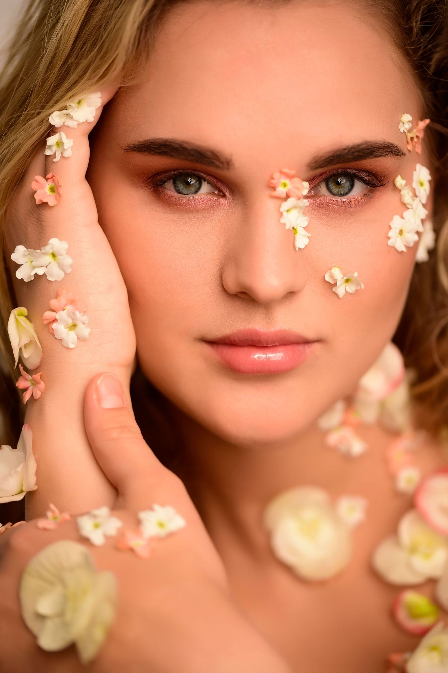 Creative beauty portrait with delicate white flower petals decorating the face against soft peach background.