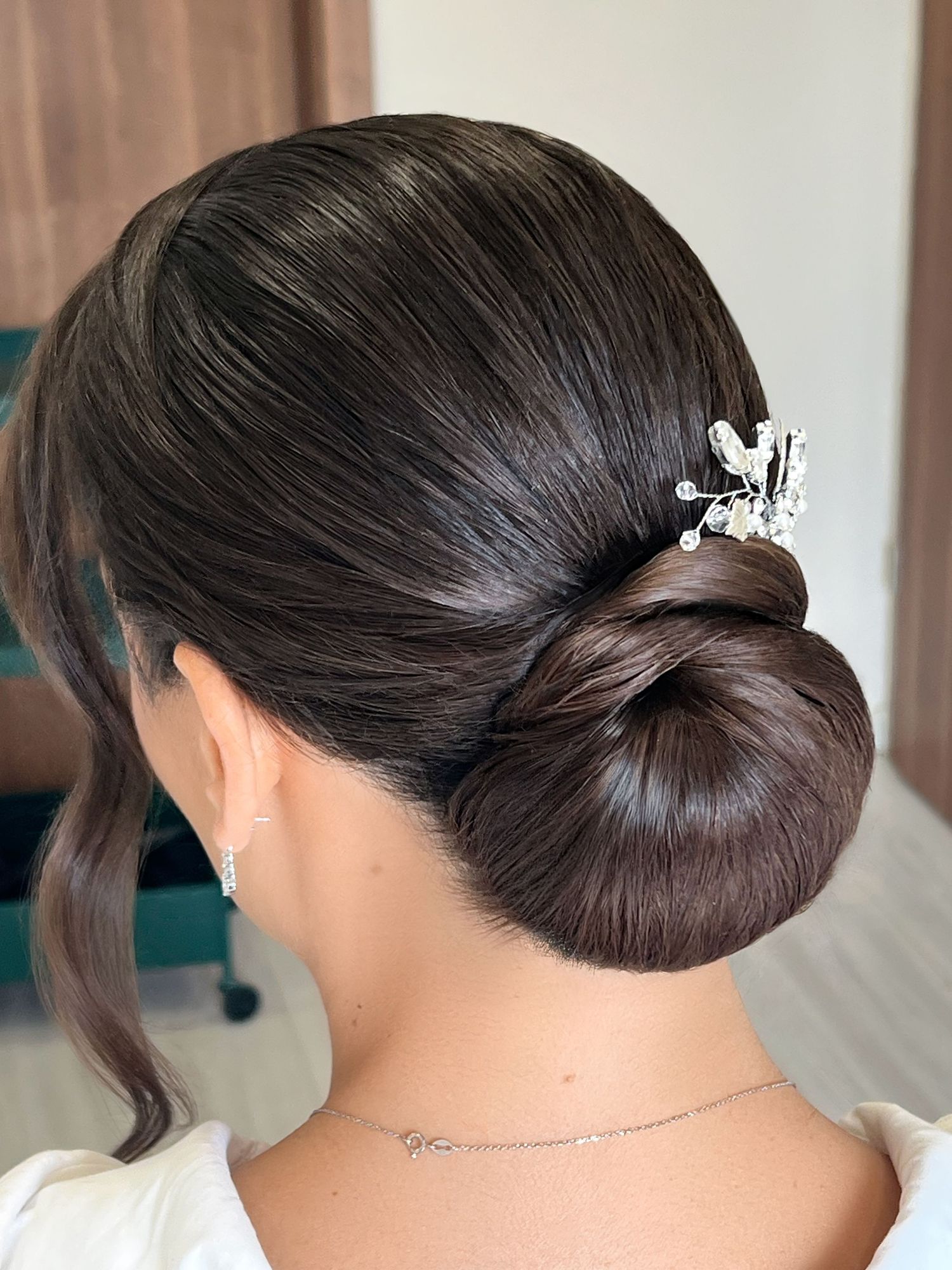 Elegant low bun updo with a decorative crystal hair pin, perfect for weddings or formal occasions.