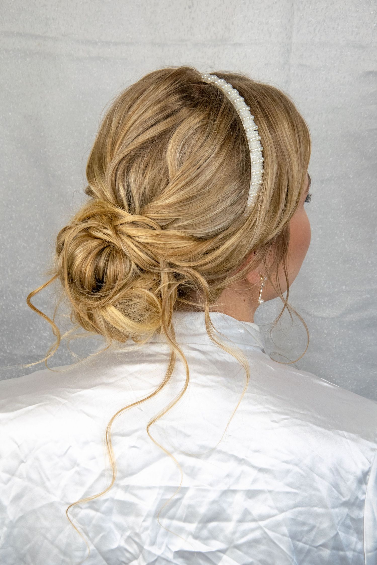 Elegant bridal updo with pearl headband and loose blonde tendrils.