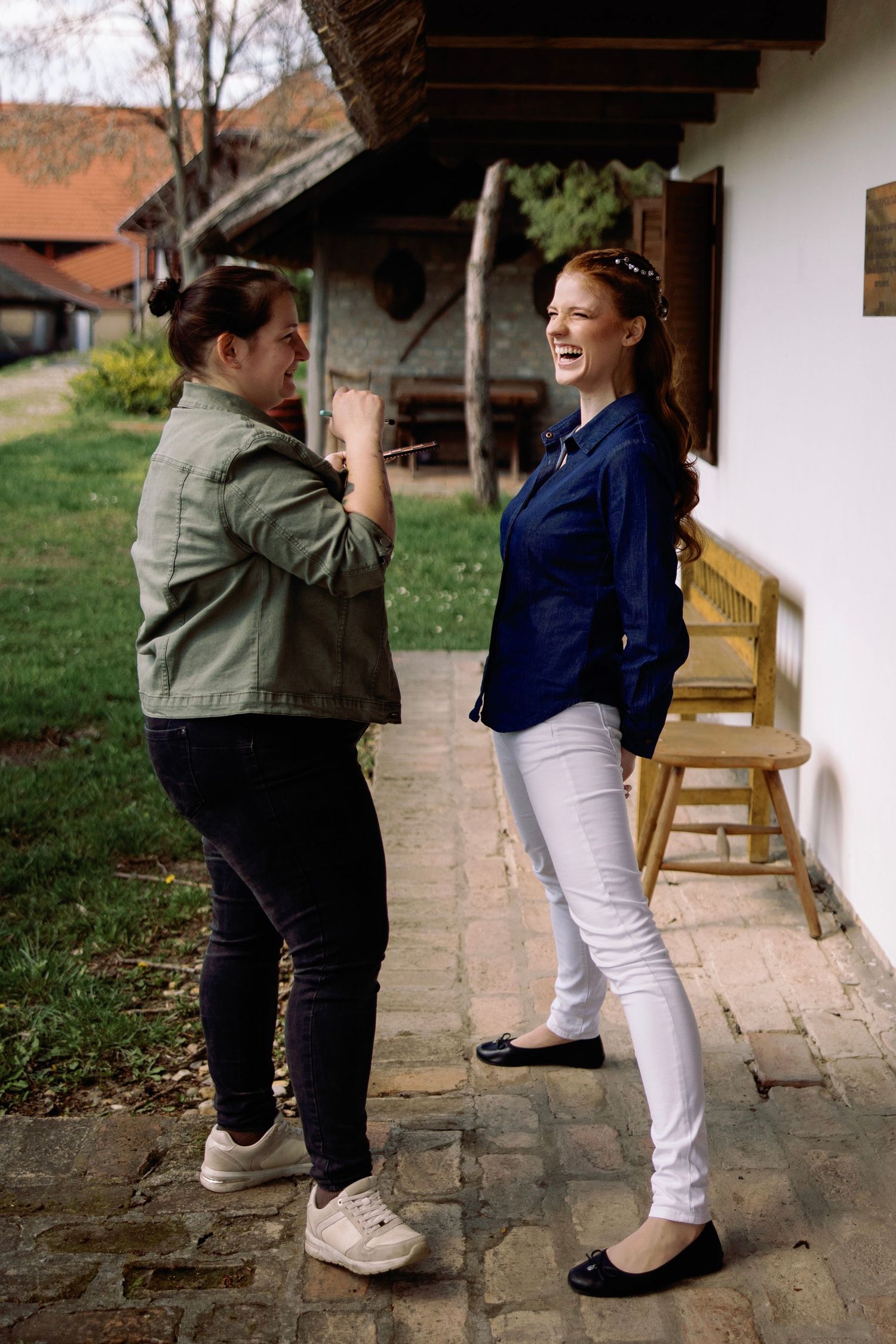 Two people share a lighthearted moment on a covered porch outside a rustic building.